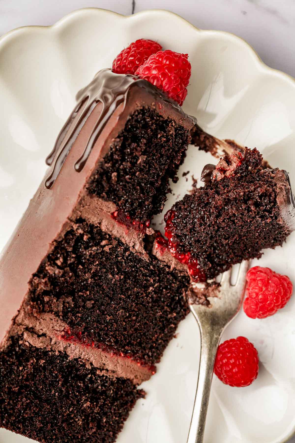 slice of chocolate cake with raspberry filling in a plate with a fork and fresh raspberries