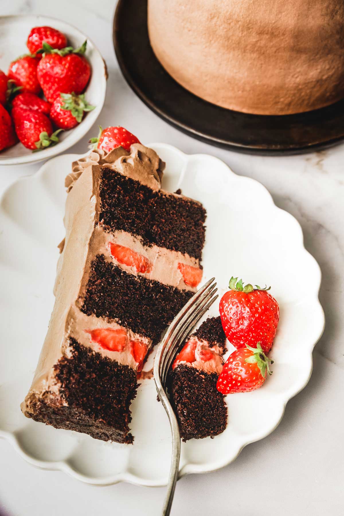 Slice of chocolate and strawberry cake on a plate and a strawberry