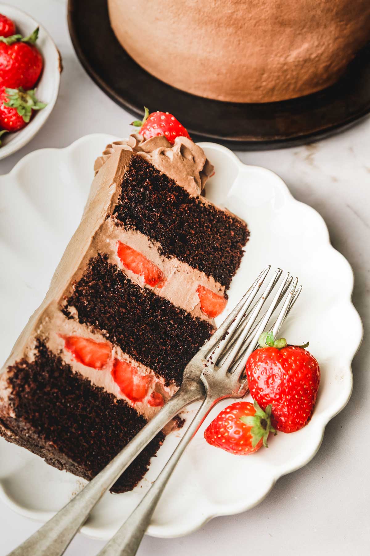 Slice of chocolate strawberry cake served on a plate with forks and strawberries