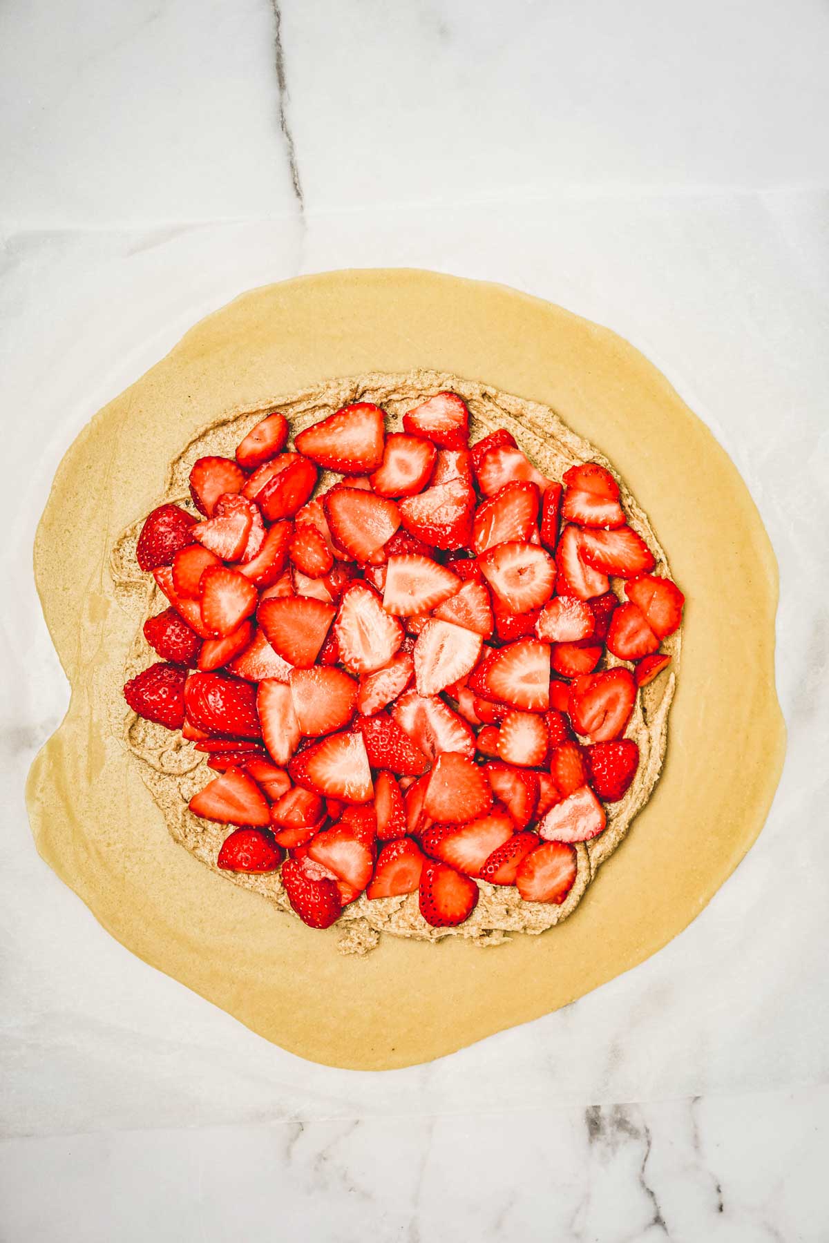 Pâte sablée étalée sur un plan de travail avec de la crème d'amande et des fraises