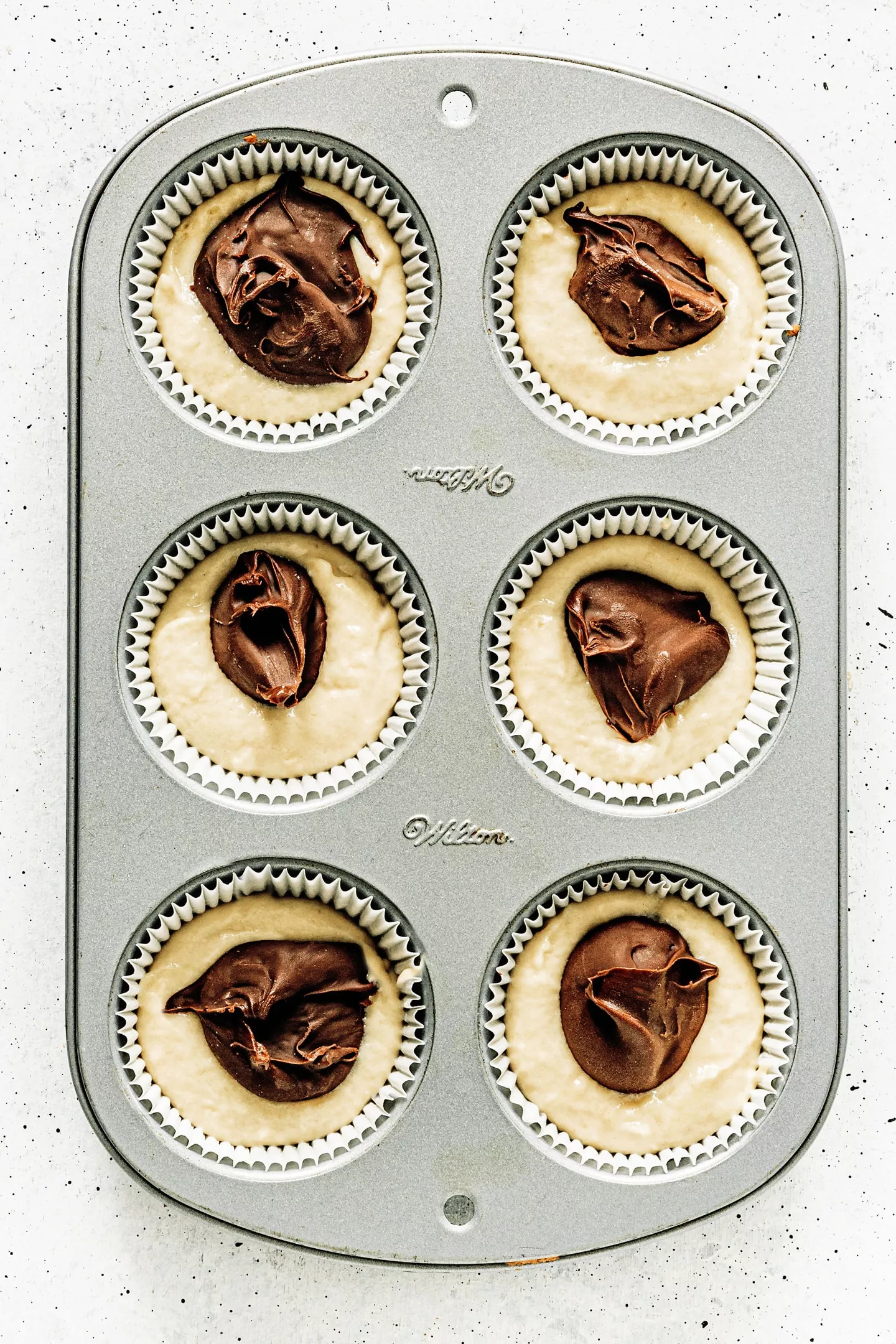 Muffin pan with muffin batter and nutella core before baking