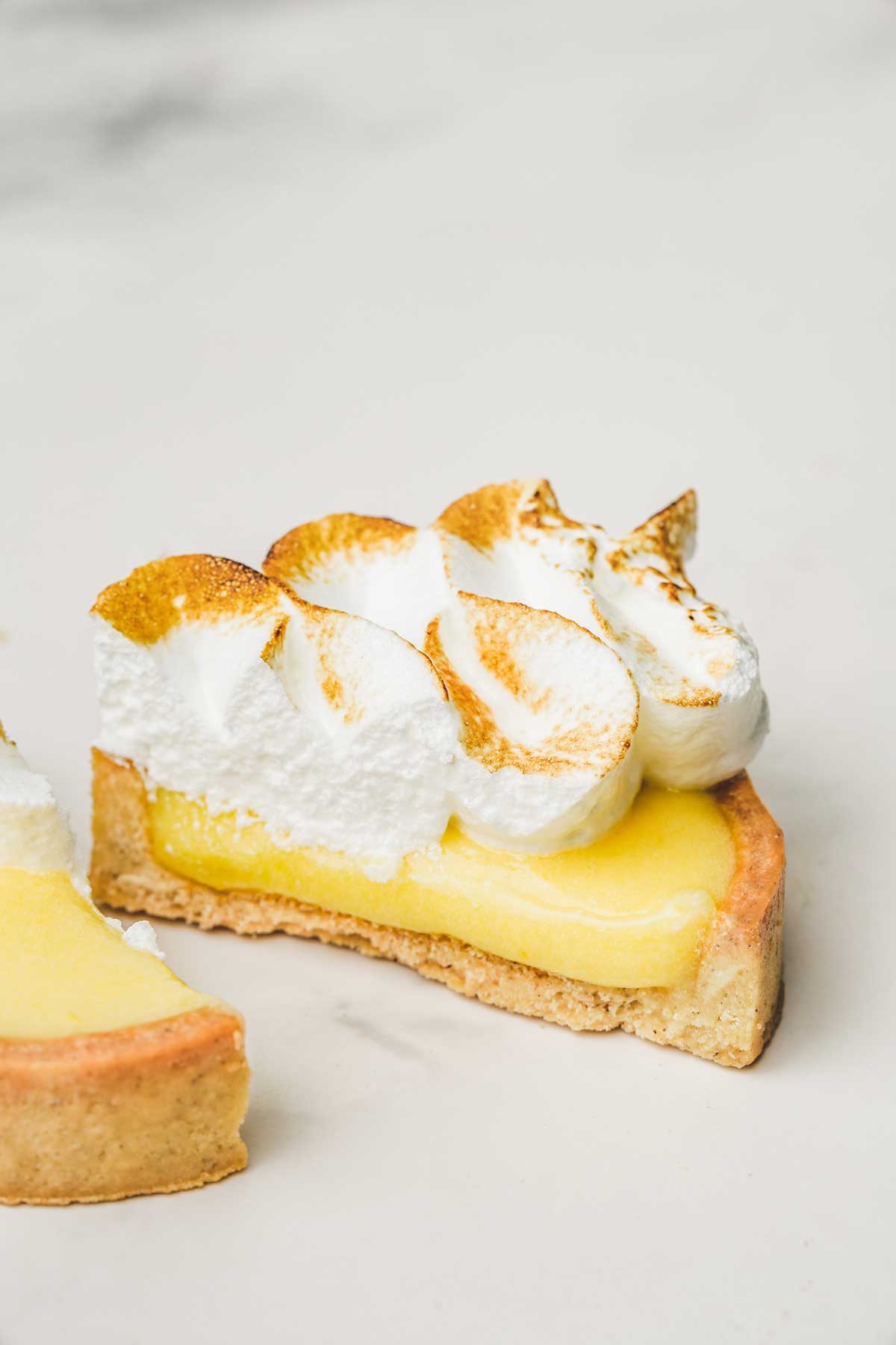 Mini lemon meringue tart cut in half showing lemon curd filling and toasted Italian meringue