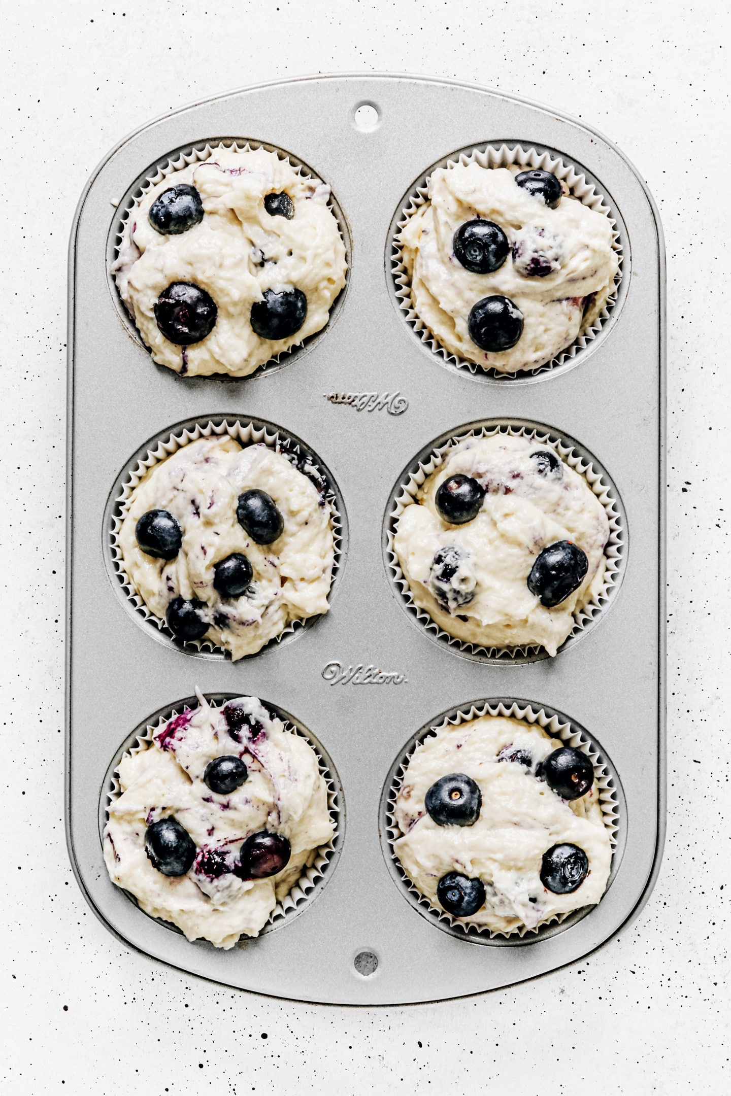 Muffin pan with muffin batter and blueberries
