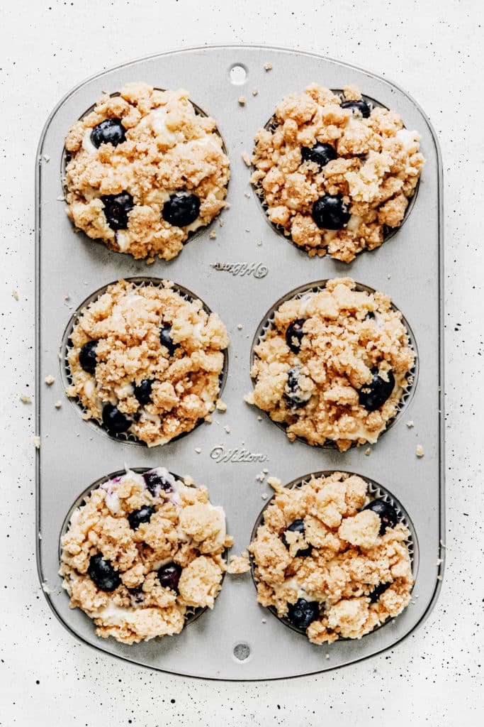 muffin pan with blueberry muffins topped with streusel