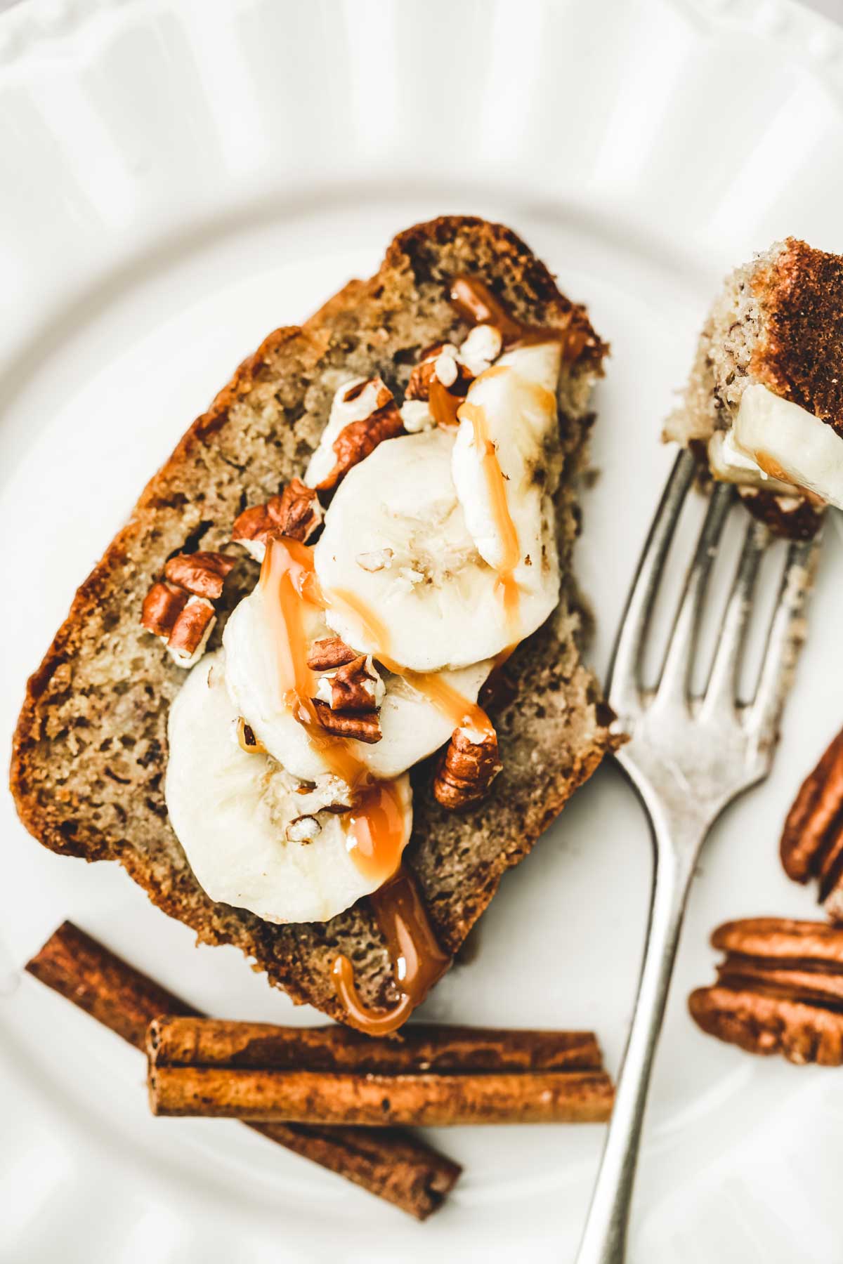Banana bread slice on a plate with banana chunks caramel sauce and chopped pecan