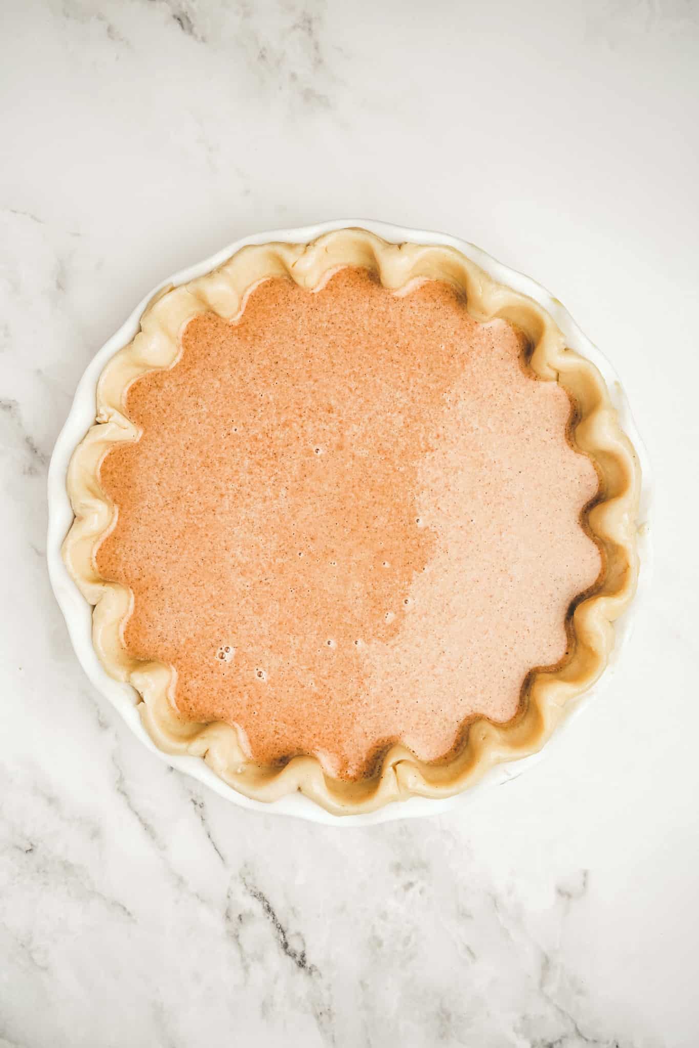 Pie pan with pie dough and pumpkin pie batter before baking