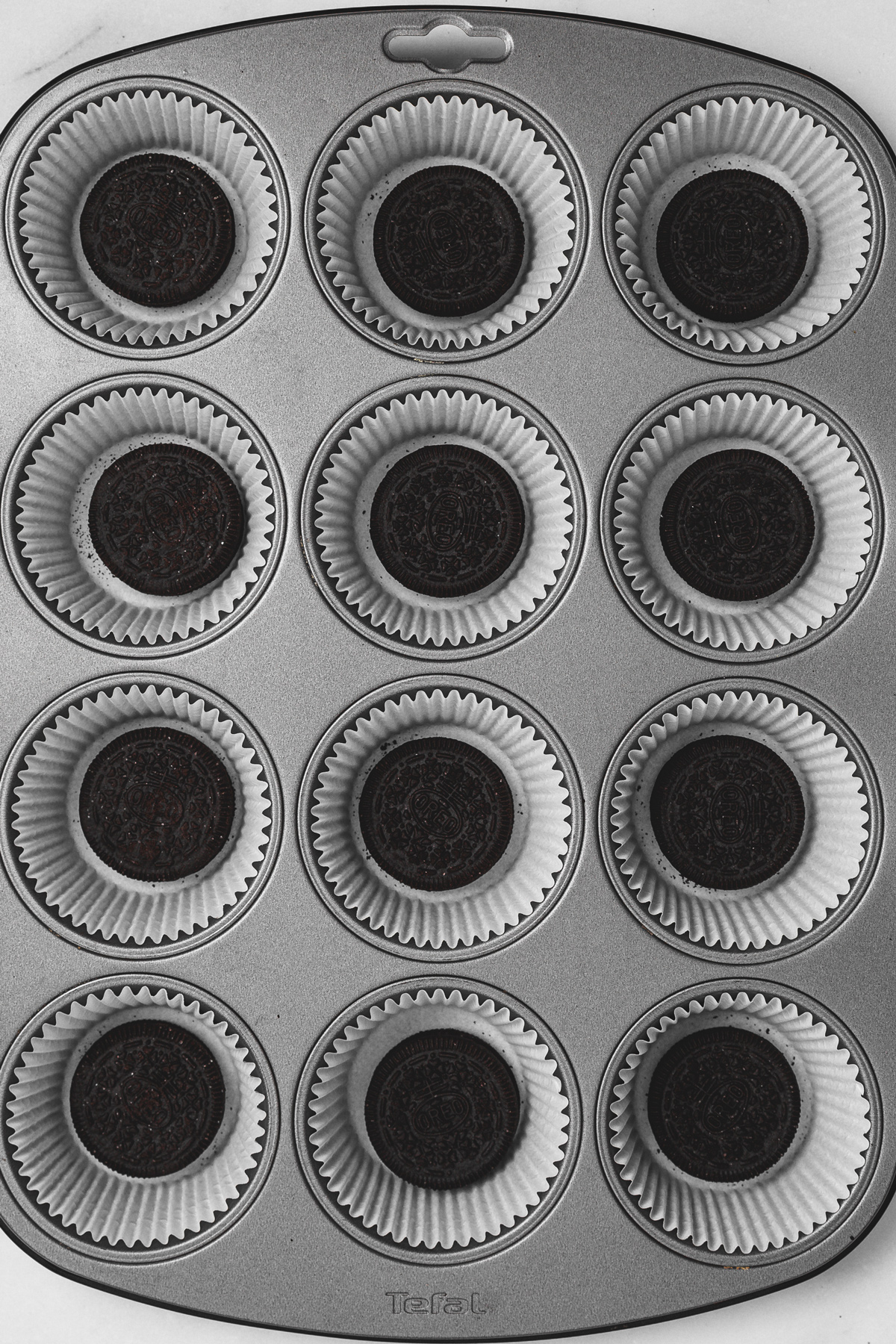 muffin pan with paper liners and whole oreo cookies