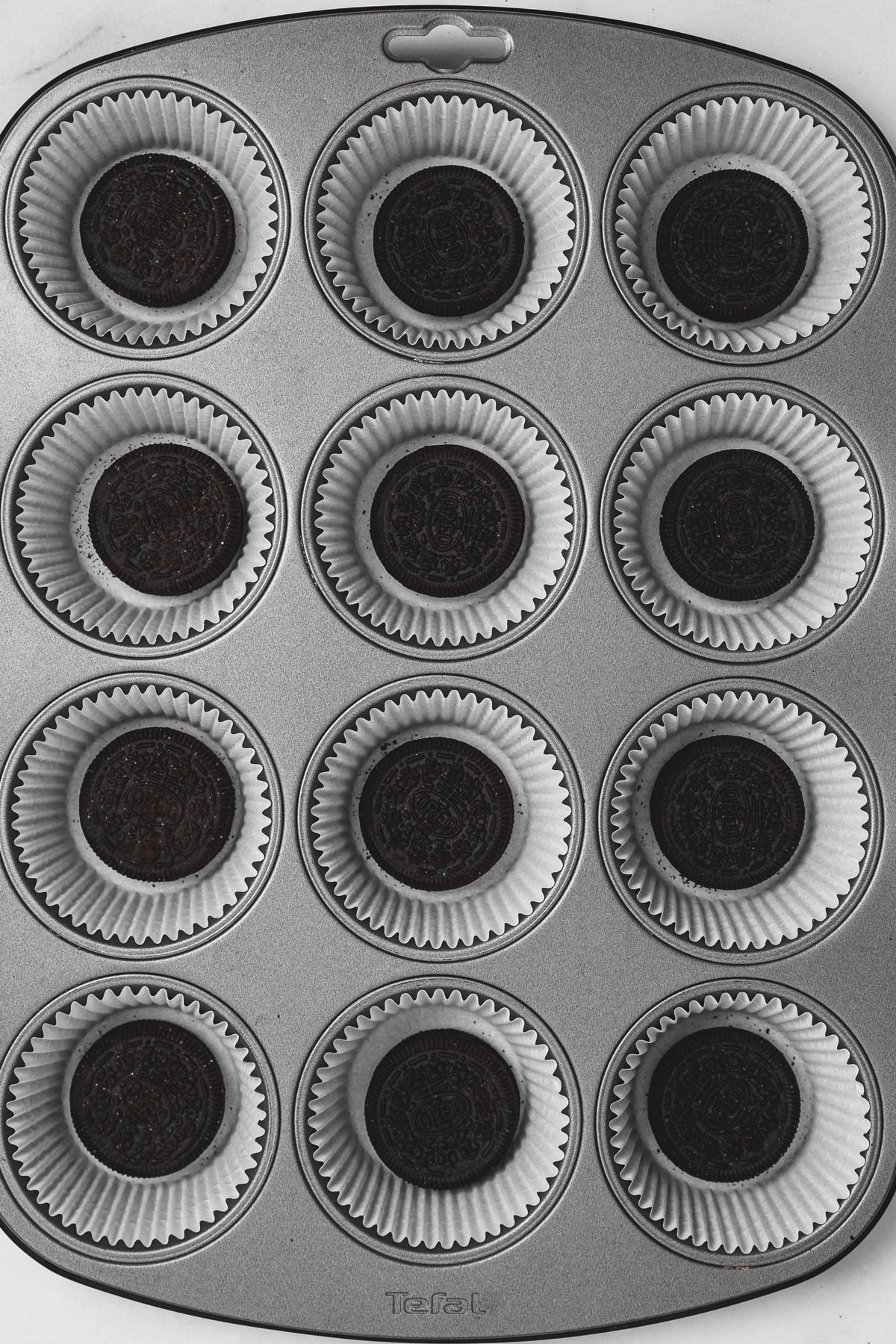 muffin pan with paper liners and whole oreo cookies