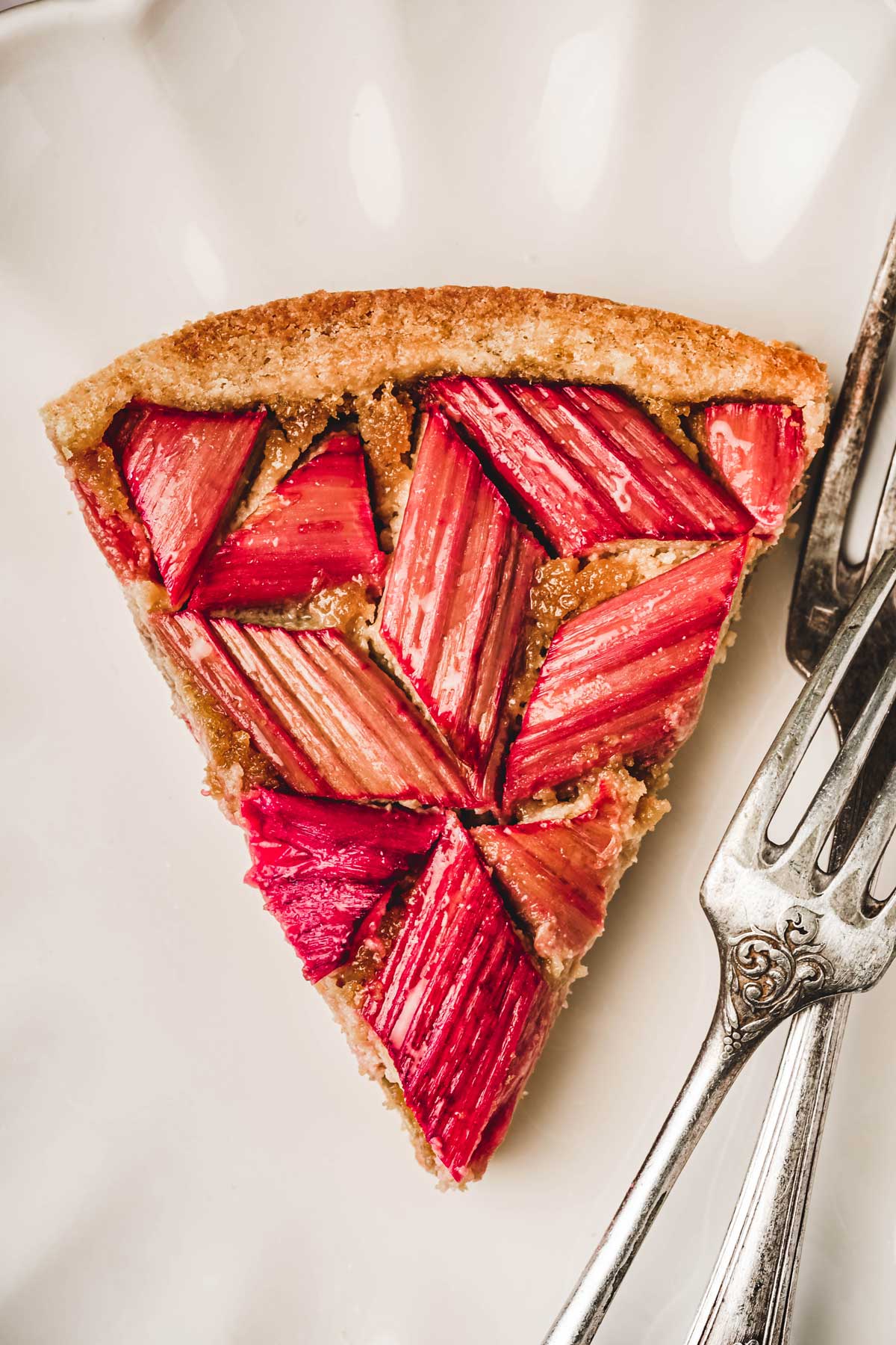 Part de tarte rhubarbe amande avec fourchettes dans une assiette à dessert