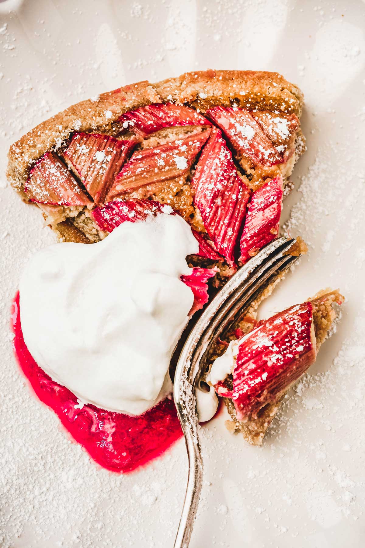 Part de tarte rhubarbe avec chantilly et compote de fruit dans une assiette avec une fourchette