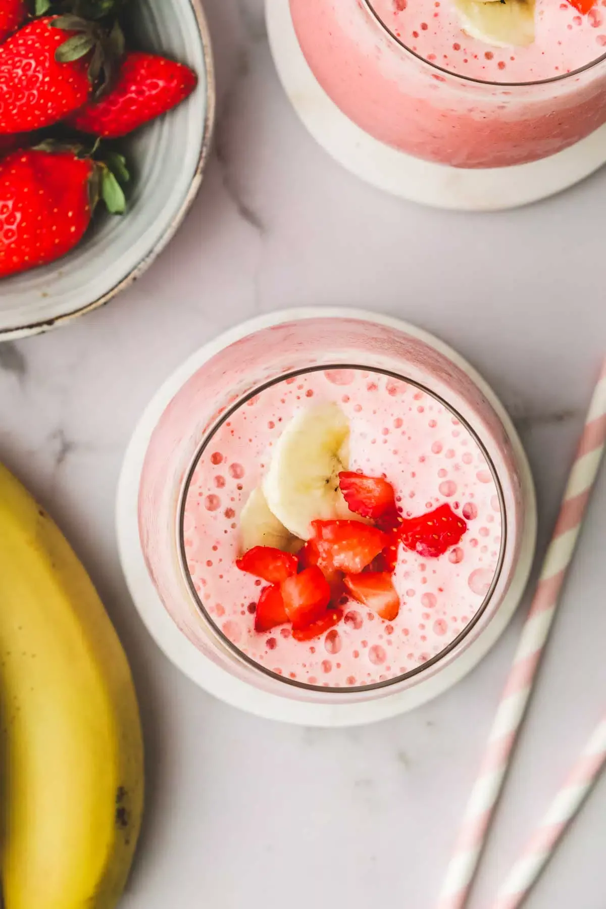 A glass of smoothie with banana pieces and strawberries
