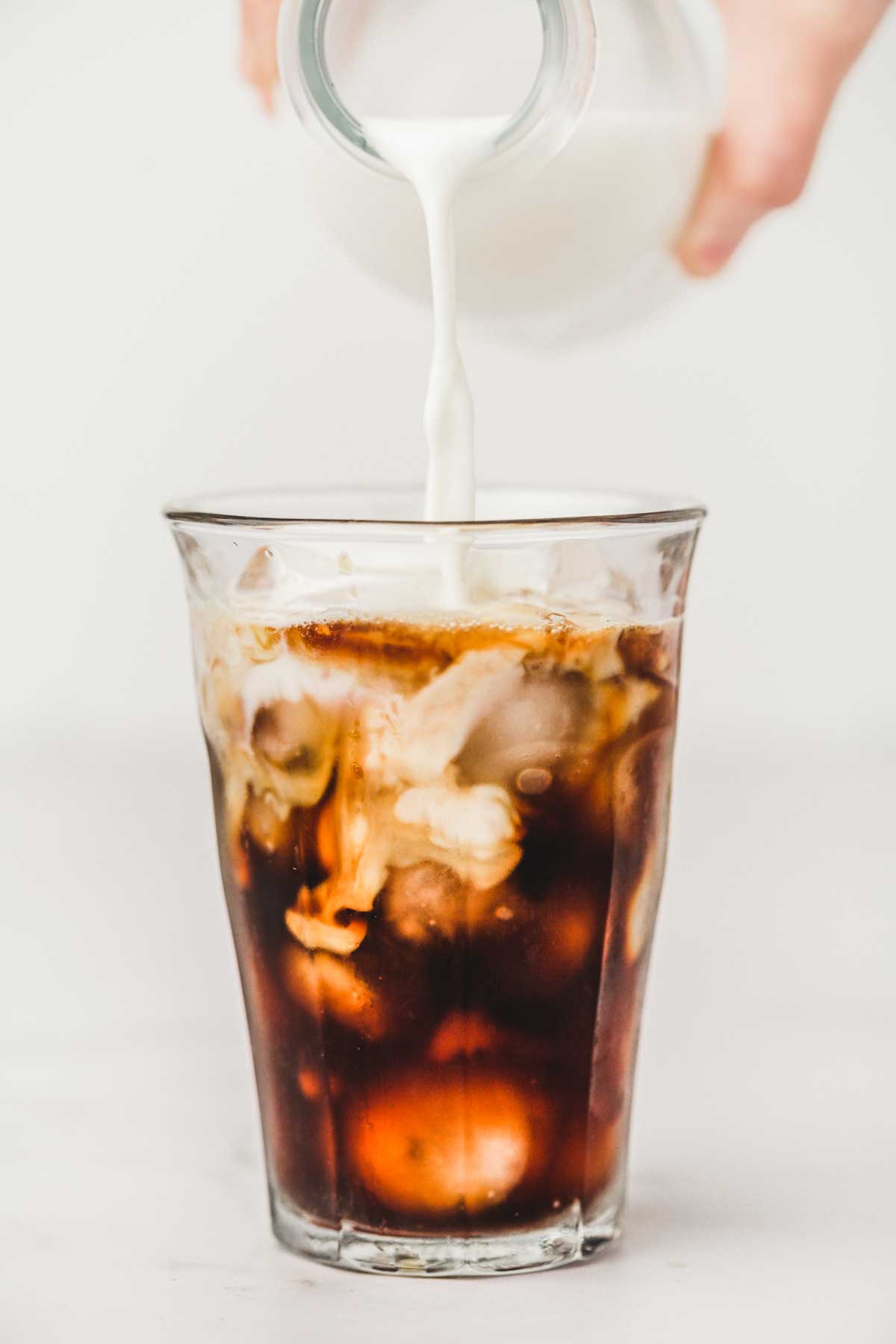 Bouteille de lait avec du lait coule dans un verre rempli de café noir et de glaçons
