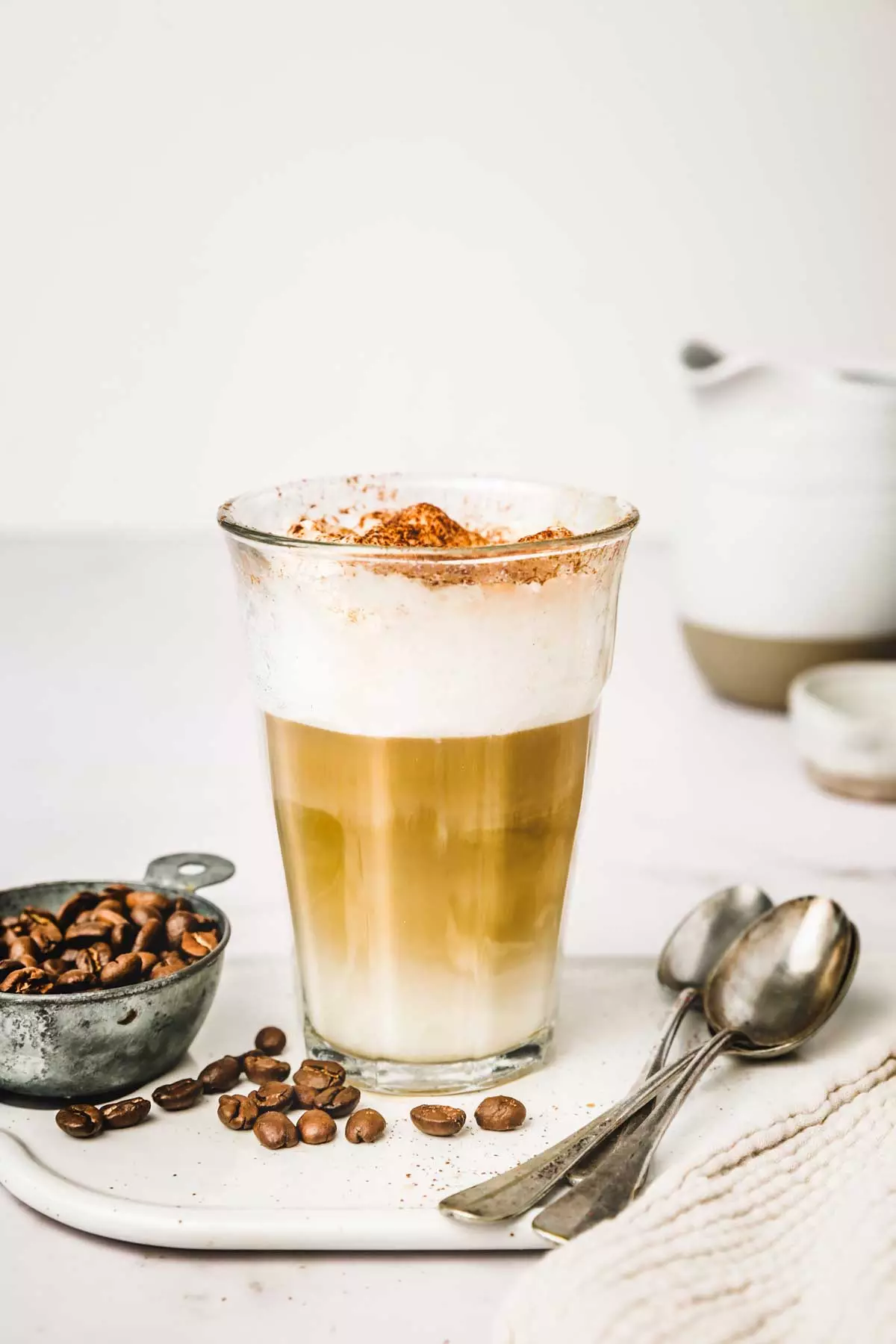 Verre avec un latte macchiato sur une table avec des grains de café et des cuillères à café