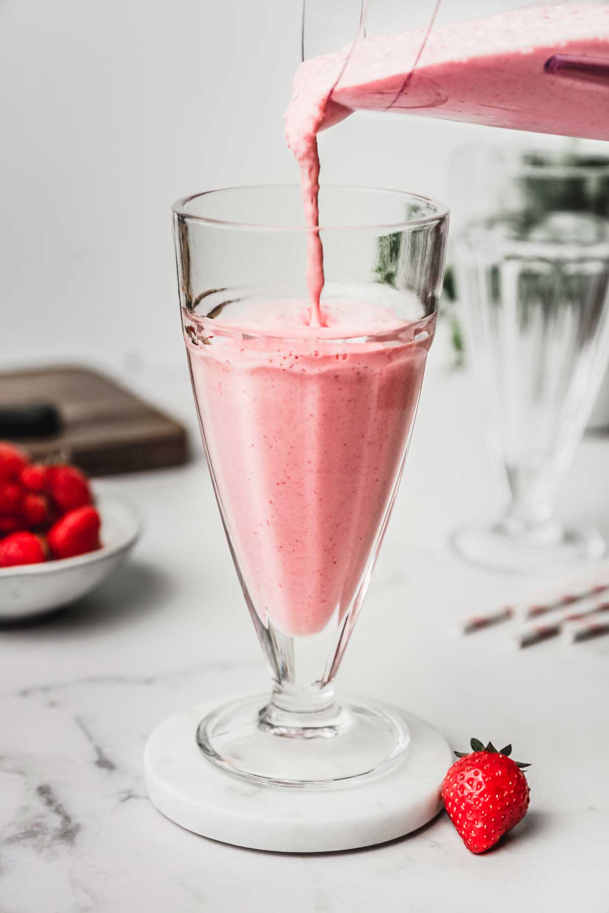 Strawberry milkshake flows into a glass 