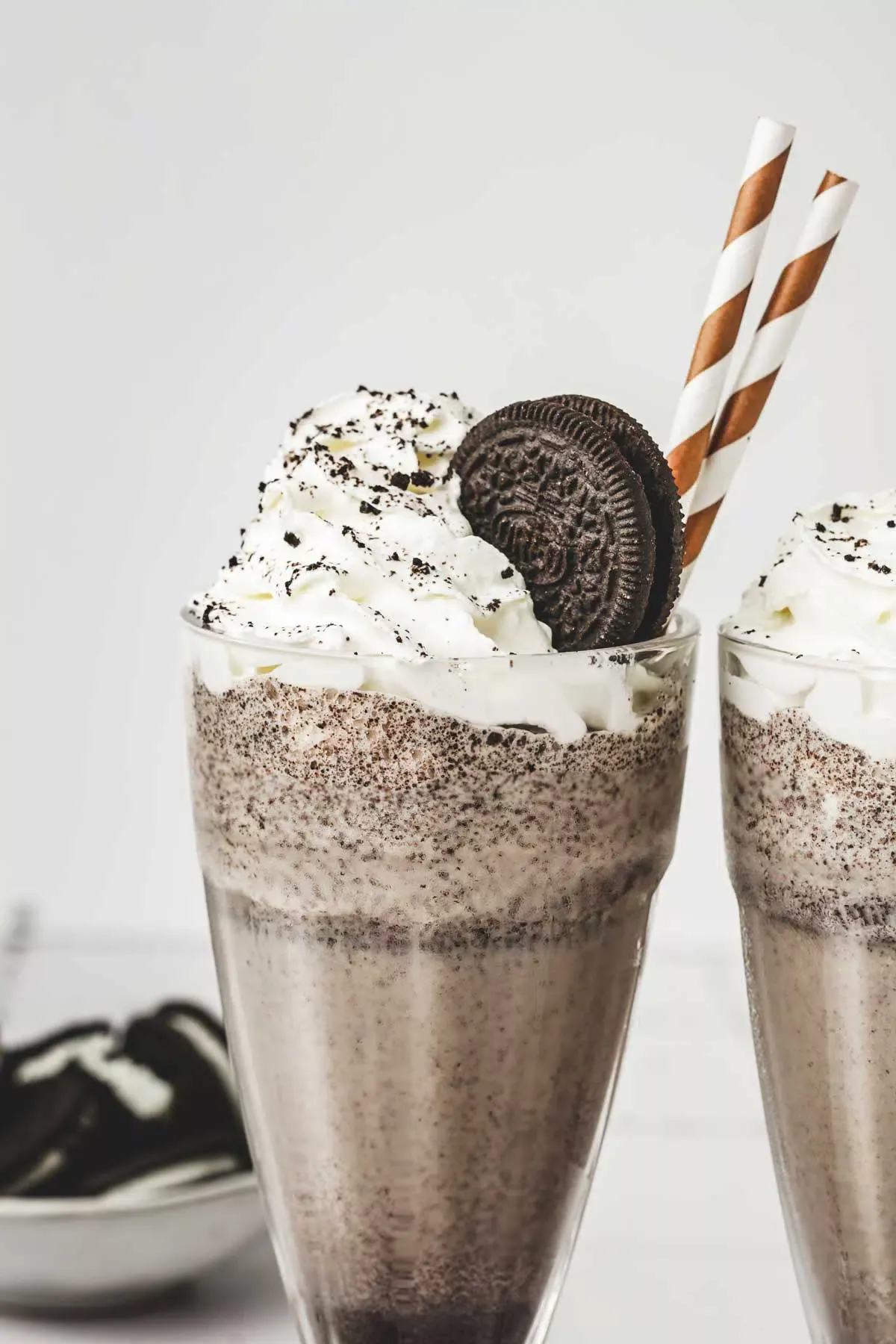 2 glasses filled with oreo milkshake with whipped cream and straws