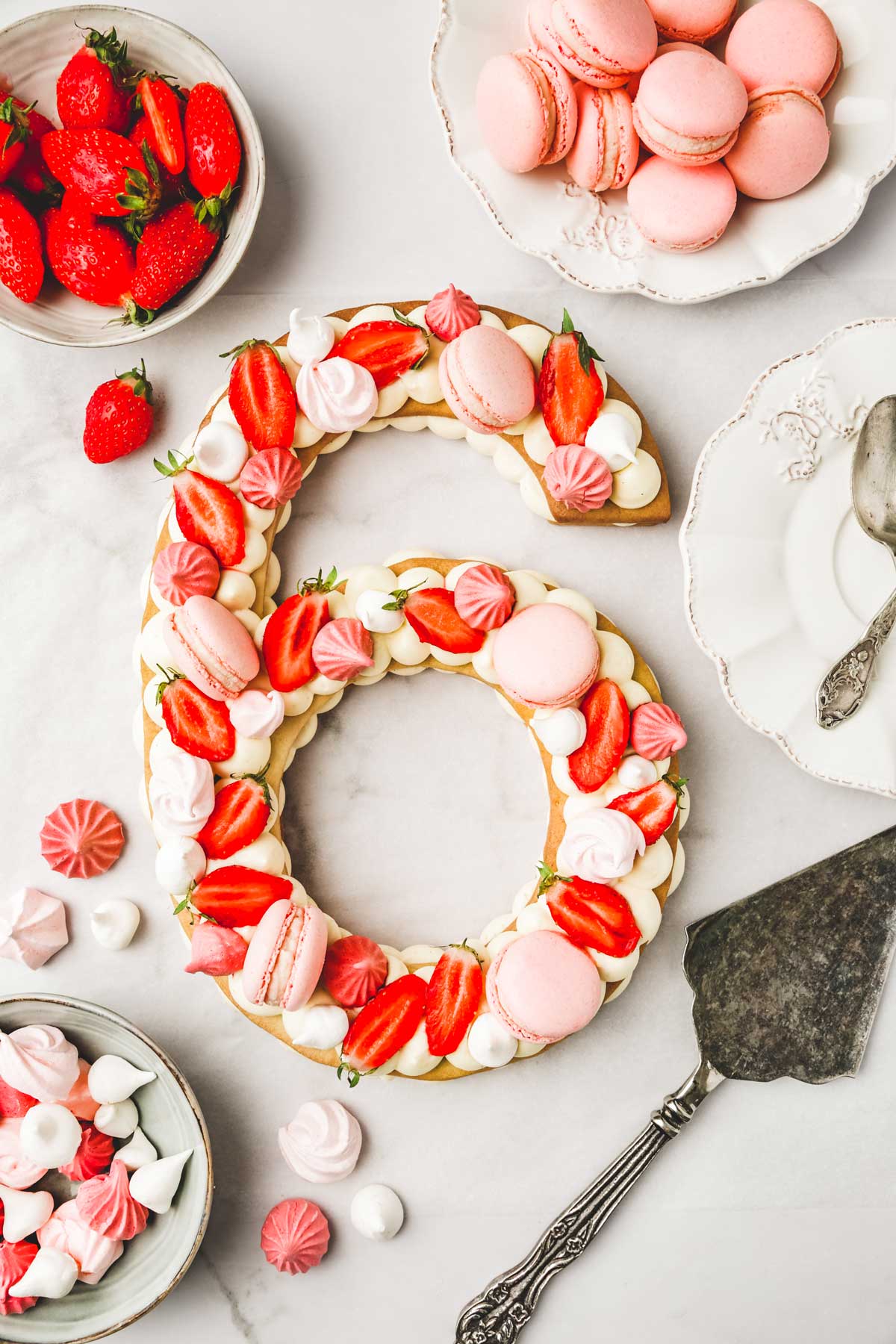 number cake on a table with strawberries, macarons and meringues