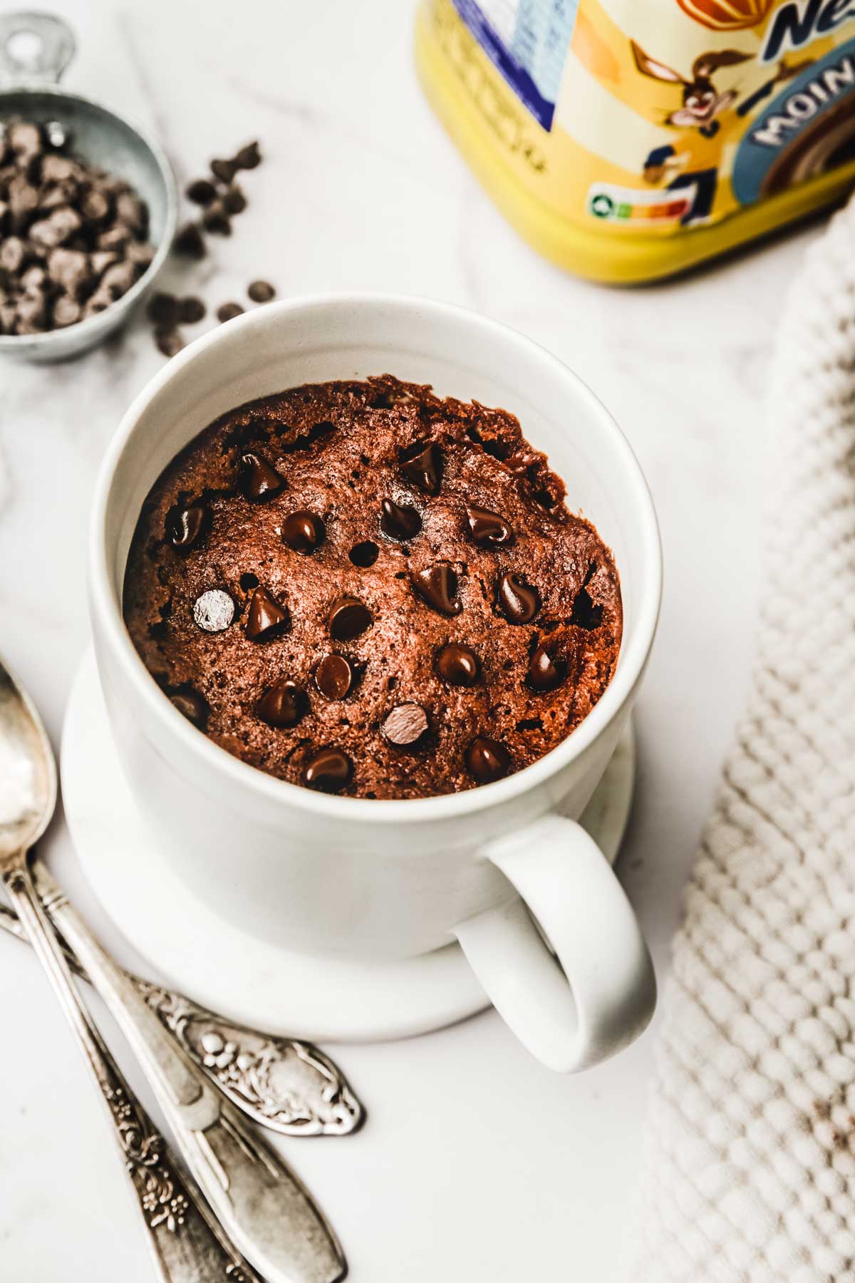Hot cocoa mug cake topped with chocolate chips and spoons