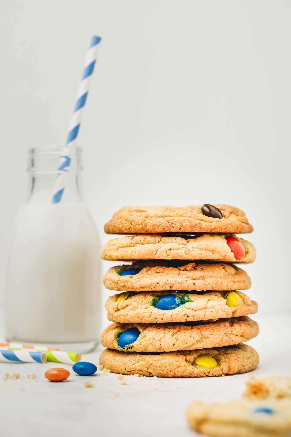 Pile of cookies on a table with m&m's with a bottle and a straw