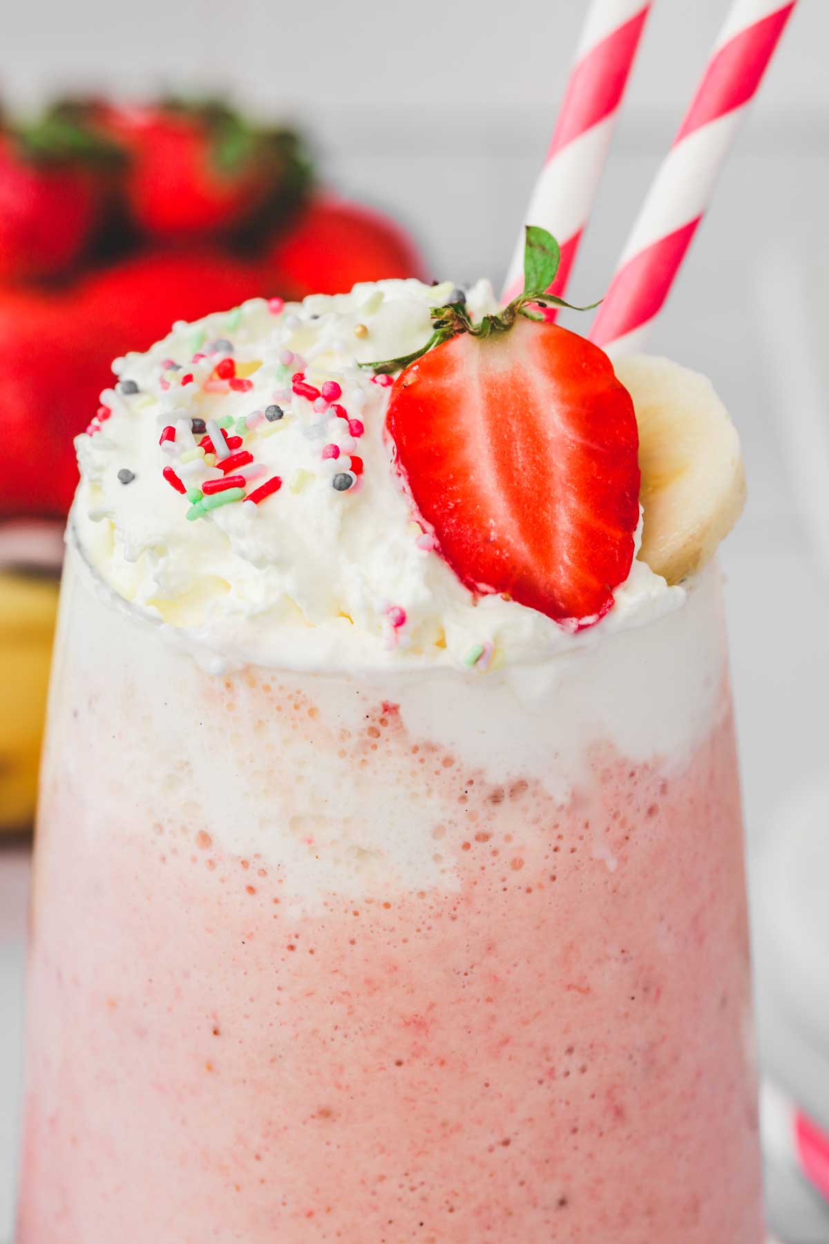 whipped cream with strawberry topping on a strawberry banana milkshake glass