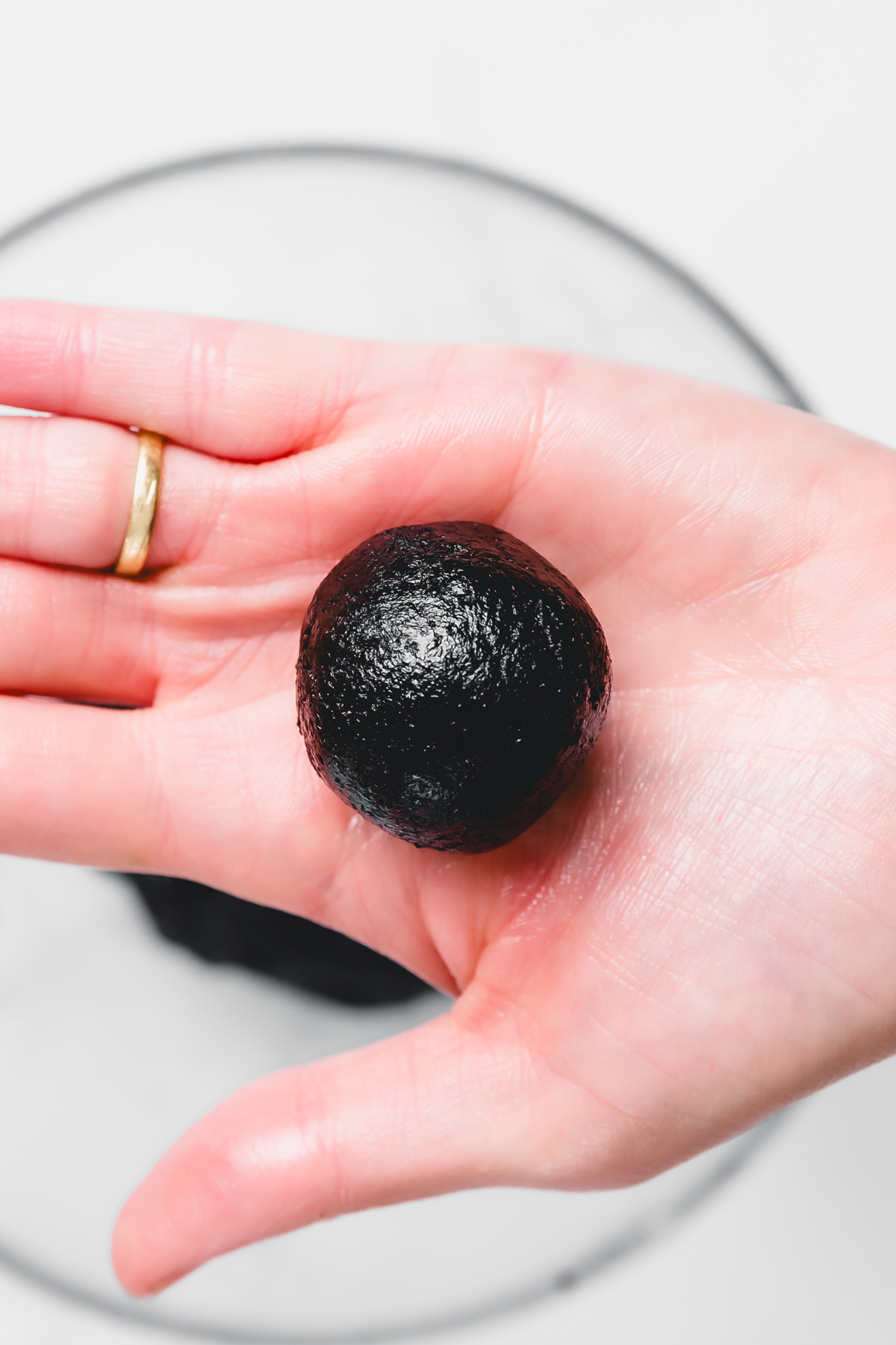 Hand holding an Oreo cake pop ball made with crushed Oreos and cream cheese before dipping in white chocolate.