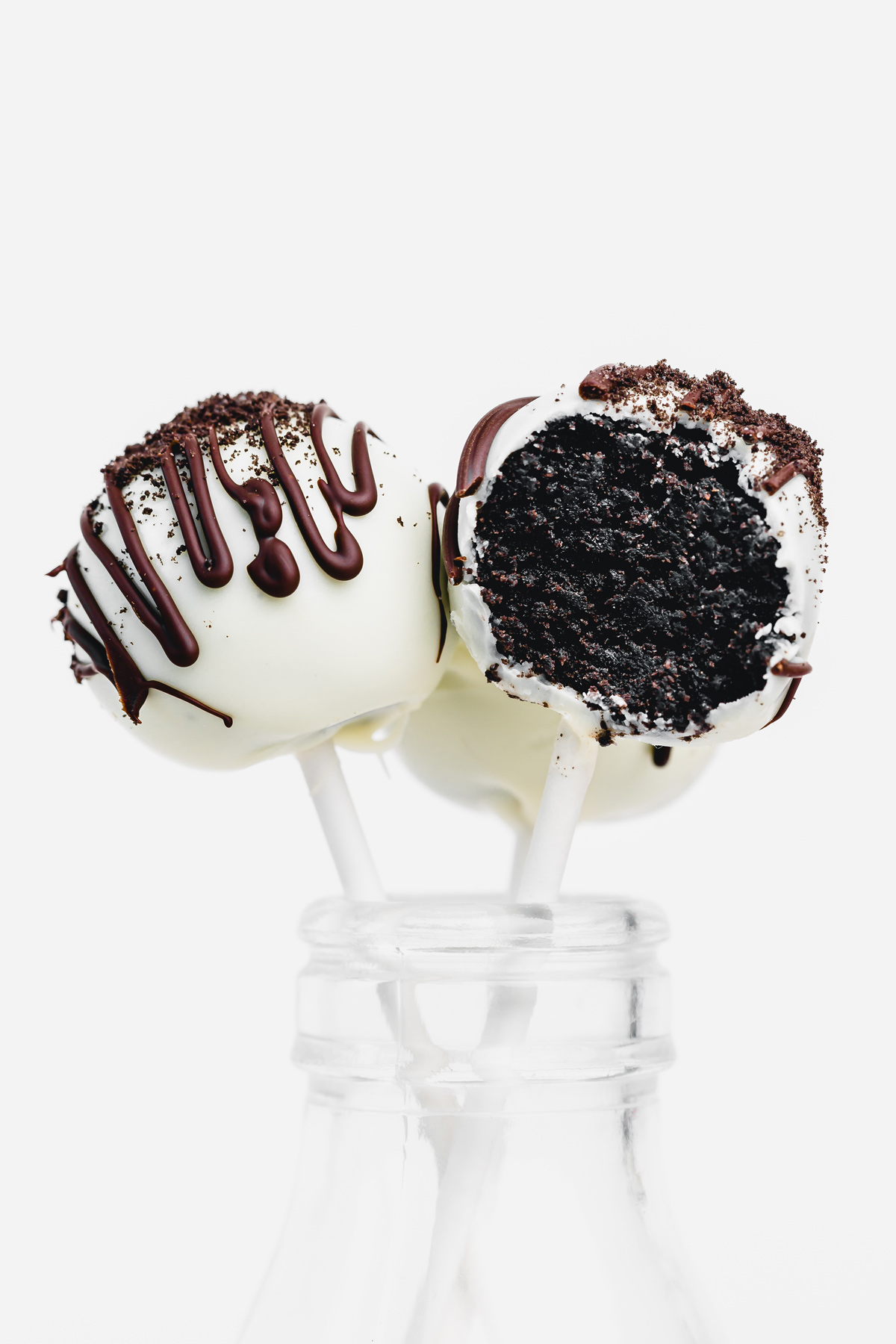 Oreo cake pop covered in white chocolate with a bite taken out, showing the creamy Oreo and cream cheese filling inside.