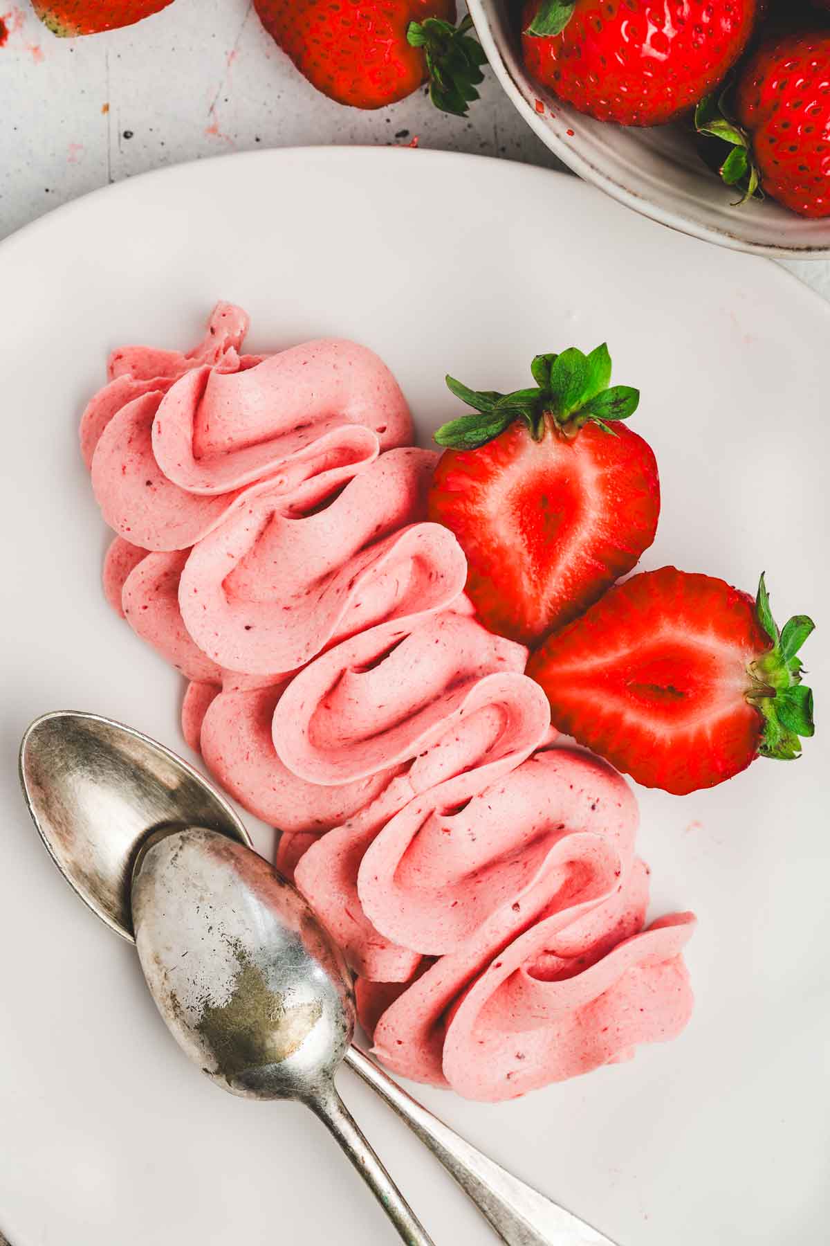 plate with fresh strawberries sliced, 2 teaspoons and pipped strawberry buttercream frosting