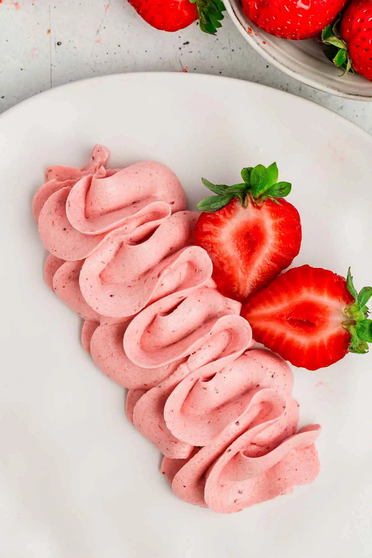 Assiette sur une table avec de la crème au beurre rose à la fraise et des fraises coupés en 2