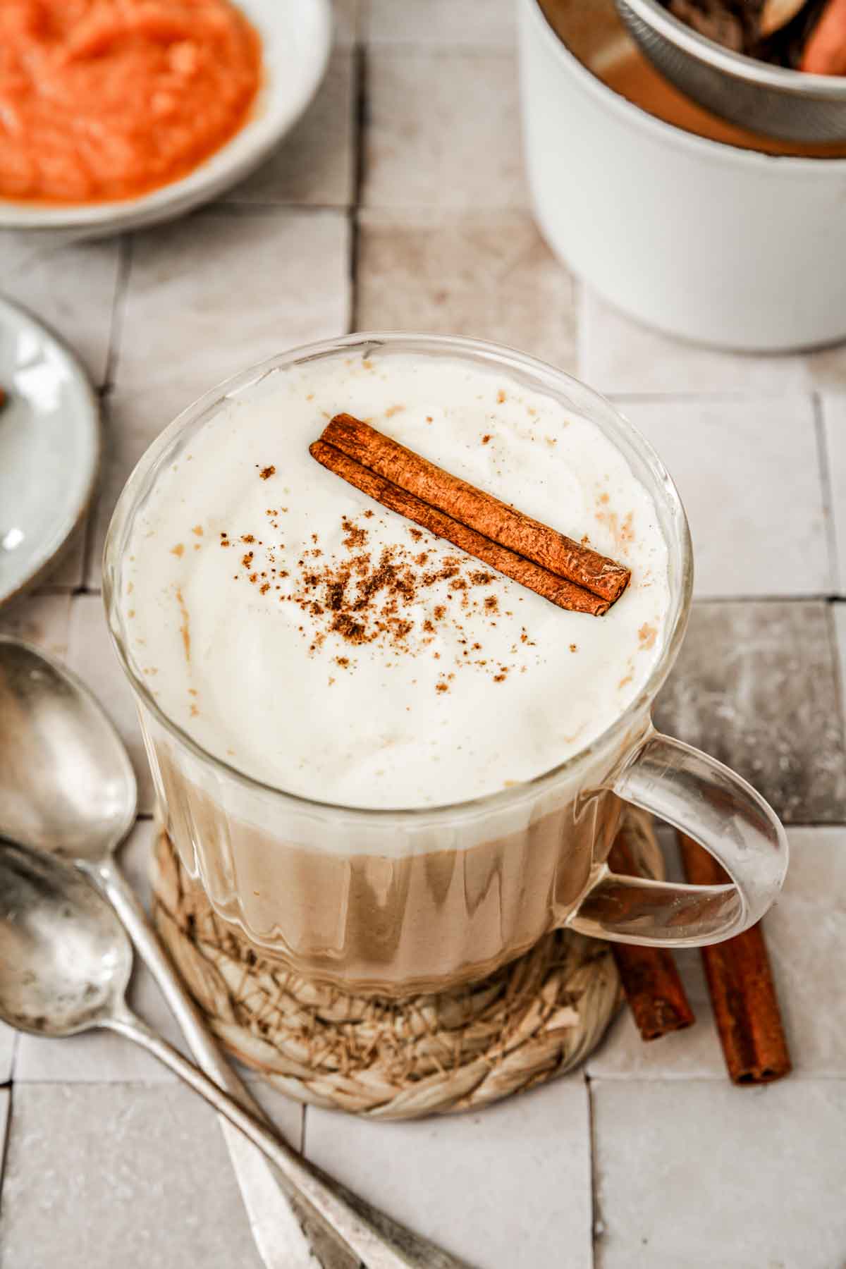 glass with pumpkin chai latte with whipped cream topping and a stick of cinnamon