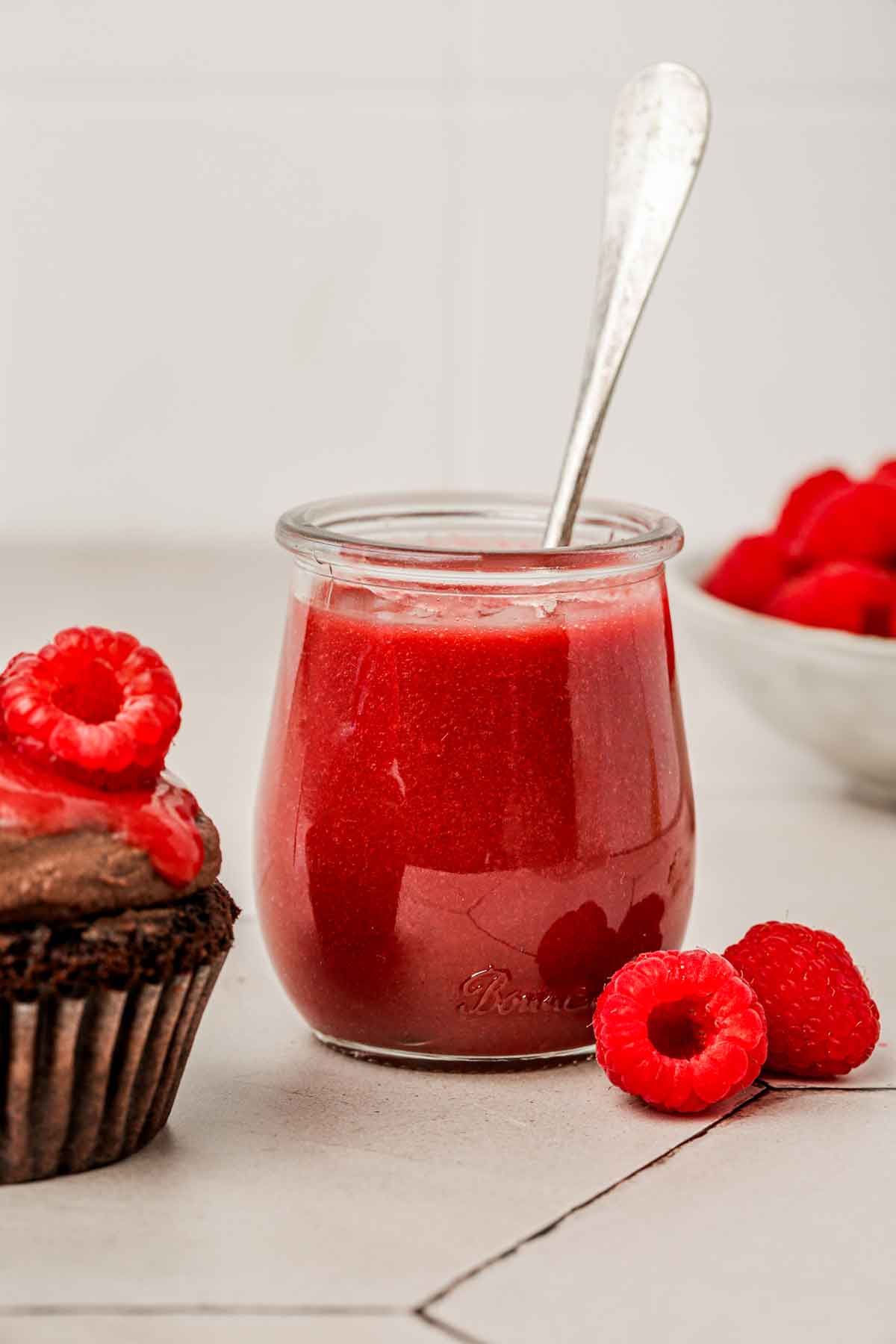 jar with raspberry coulis on a table with fresh raspberries