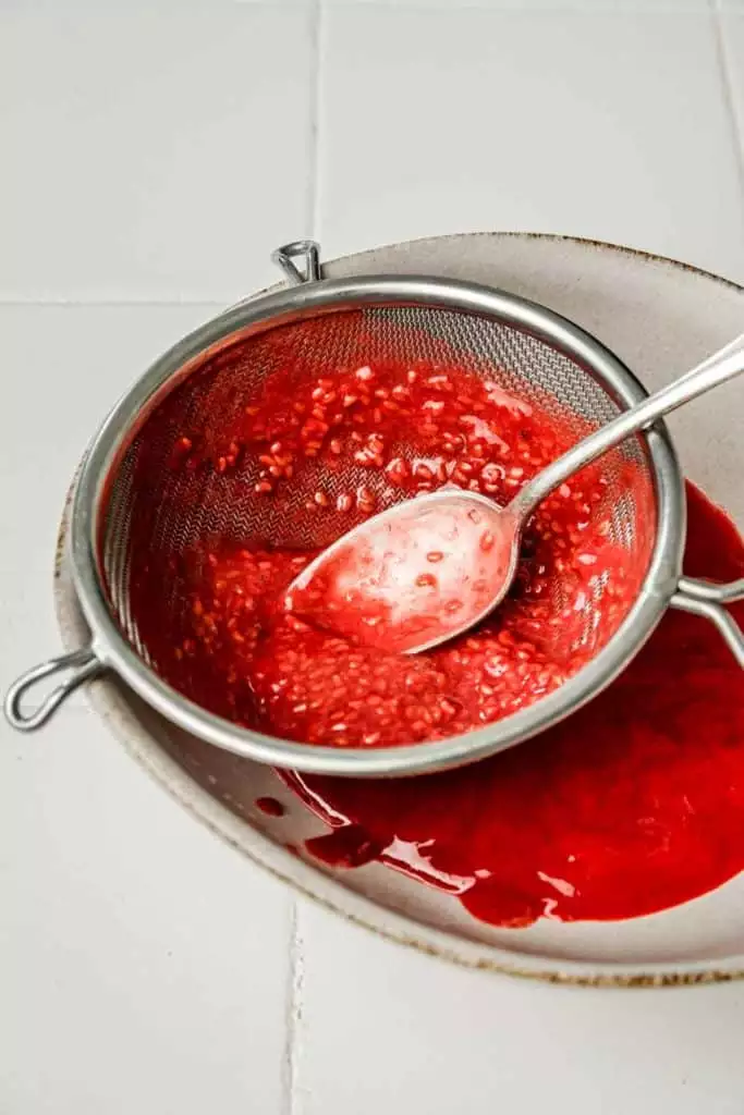 straining raspberry sauce through a fine mesh sieve