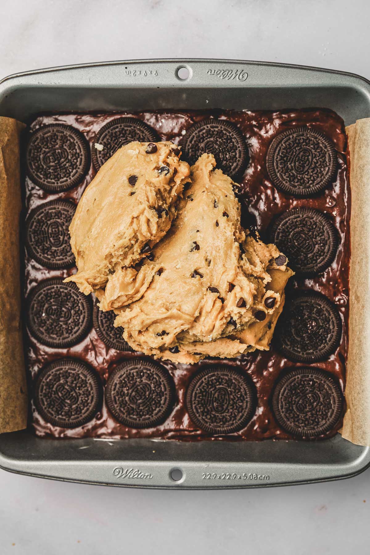 square pan with cookie dough over oreo cookies