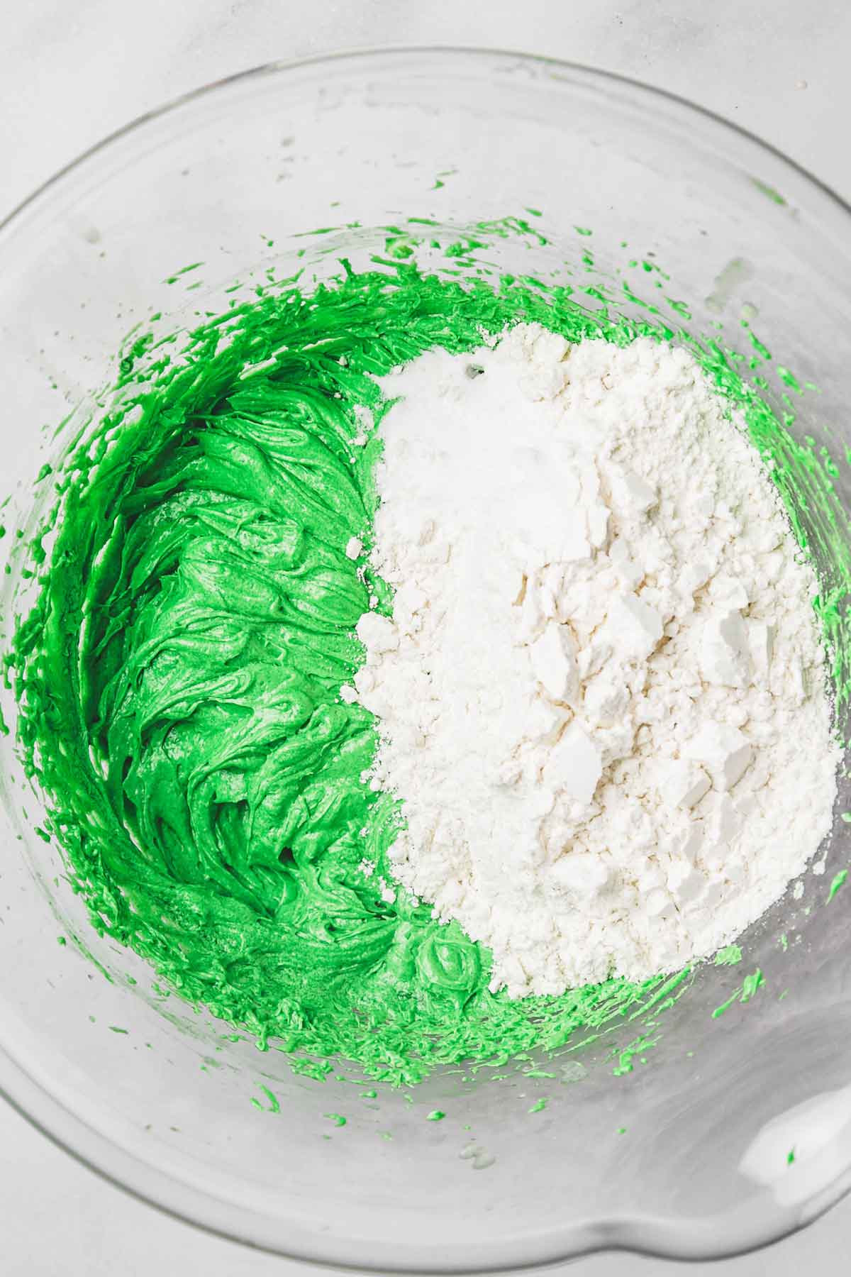 large mixing bowl with green cookie batter and flour mixture