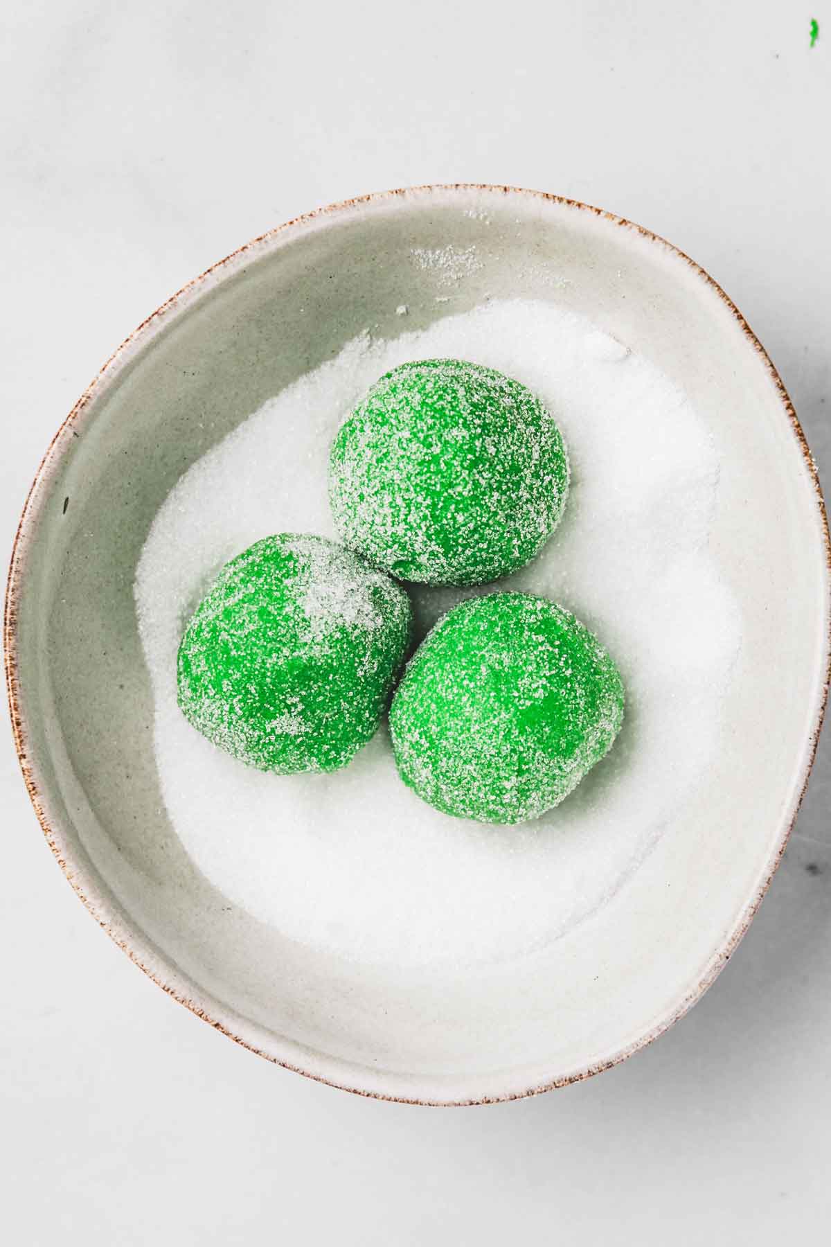 bowl with green cookie dough balls and granulated sugar