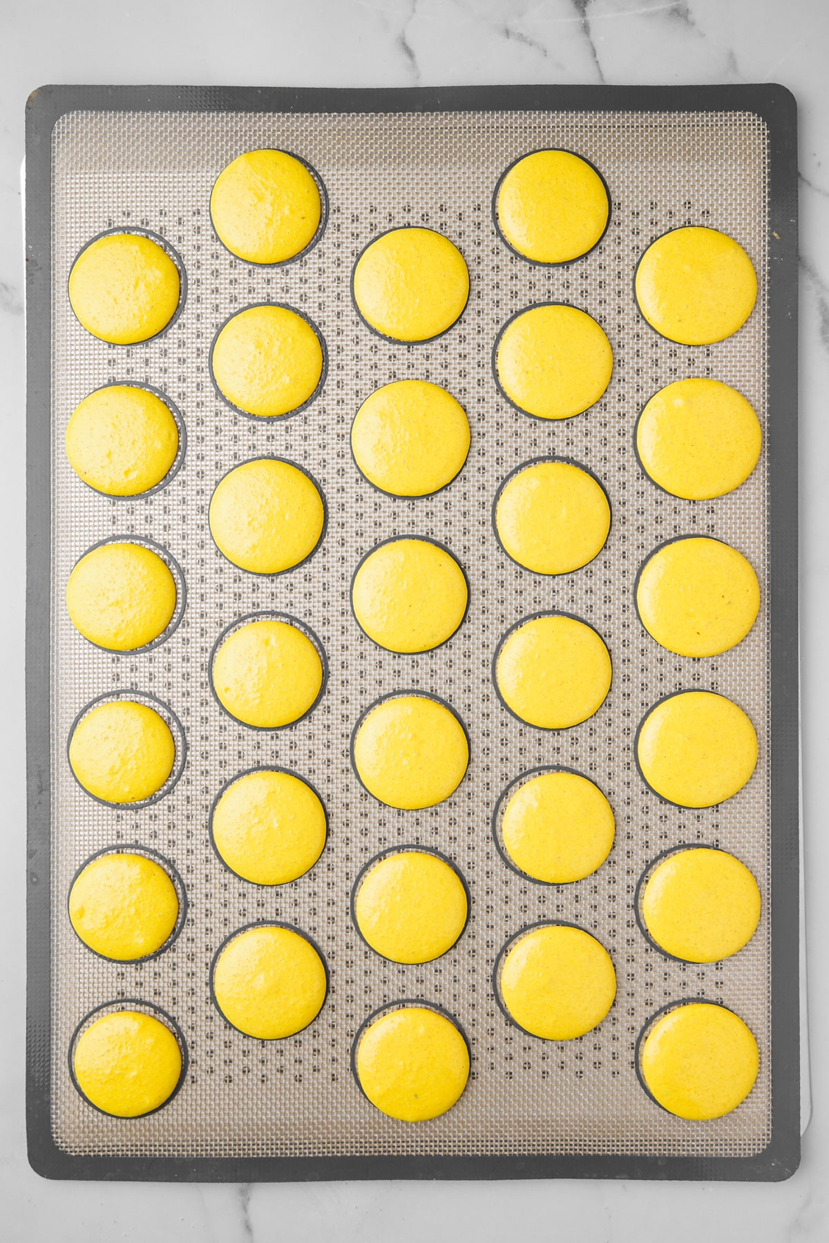 silicone baking mat with lemon macarons pipped