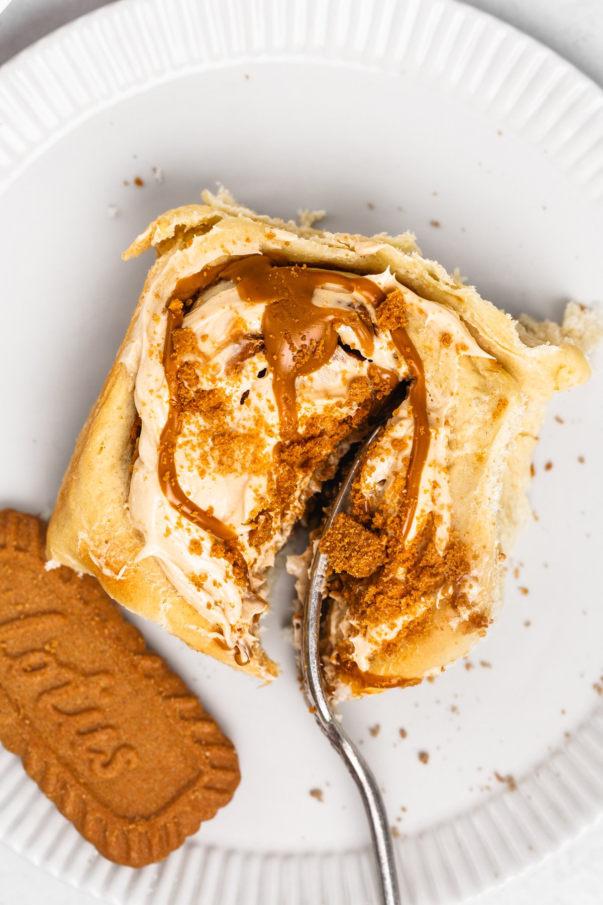 Fork slicing into a gooey Biscoff cinnamon roll on a plate