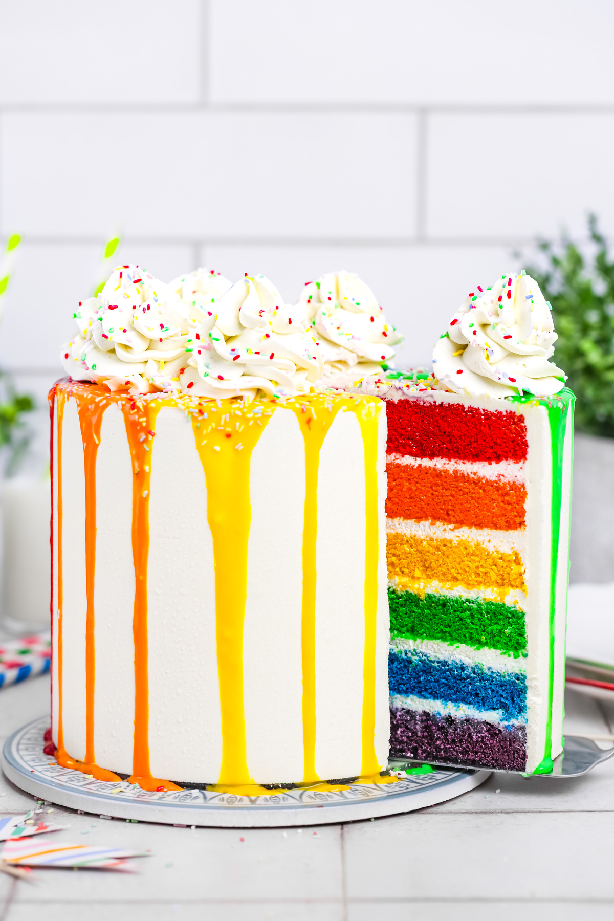 Rainbow cake on a cake stand with one slice cut out