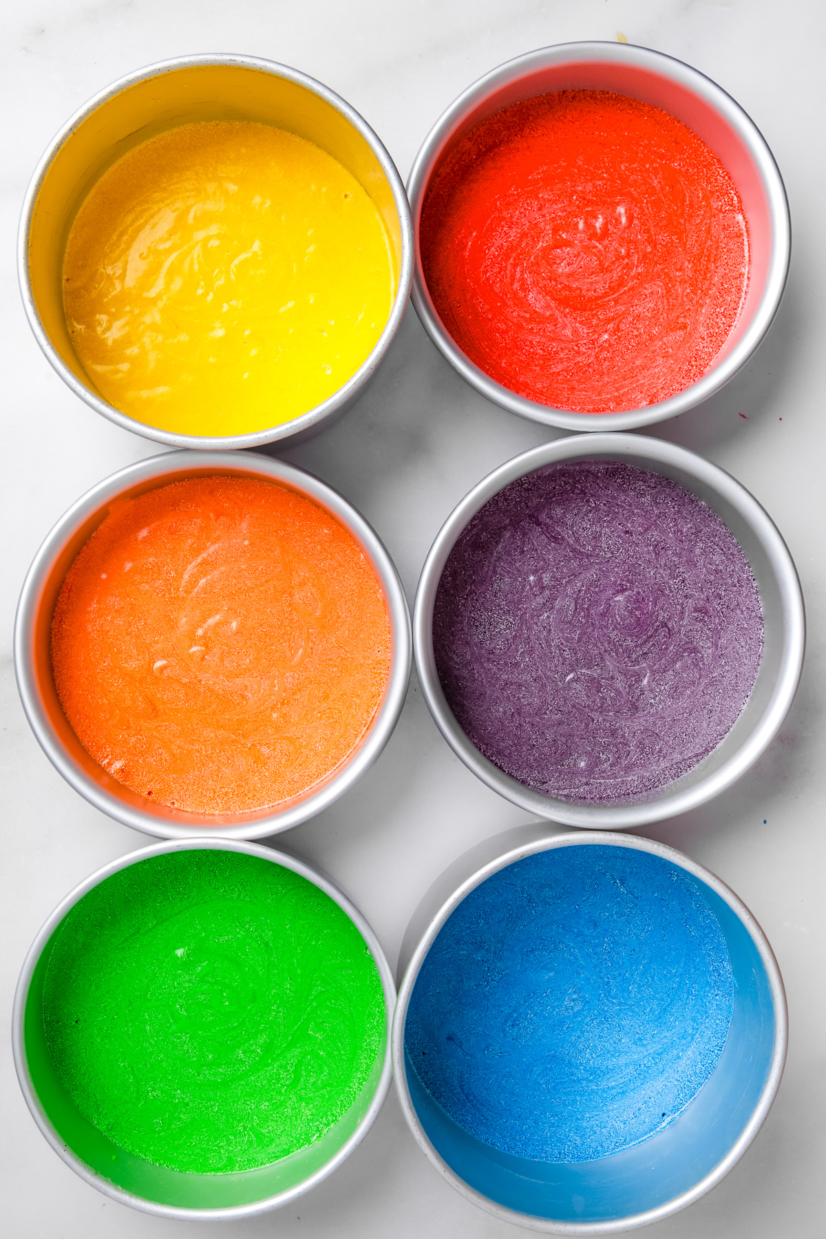 Cake pans filled with colorful rainbow cake batter