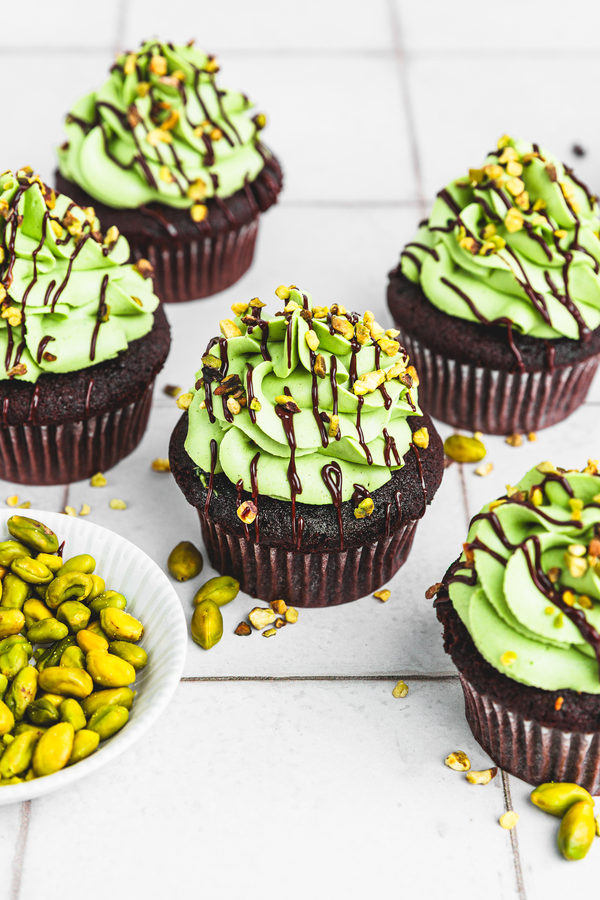 Dubai chocolate cupcakes on a table topped with pistachio ganache and dark chocolate drizzle