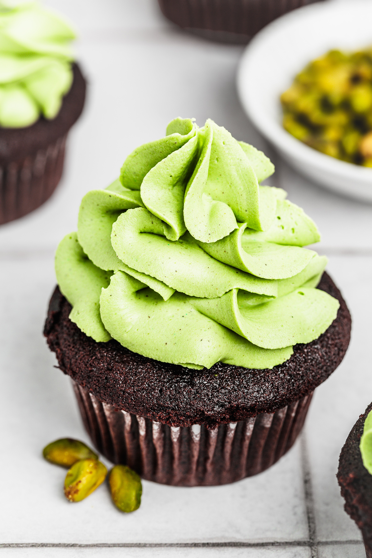 Chocolate cupcakes topped with pistachio ganache frosting on a table