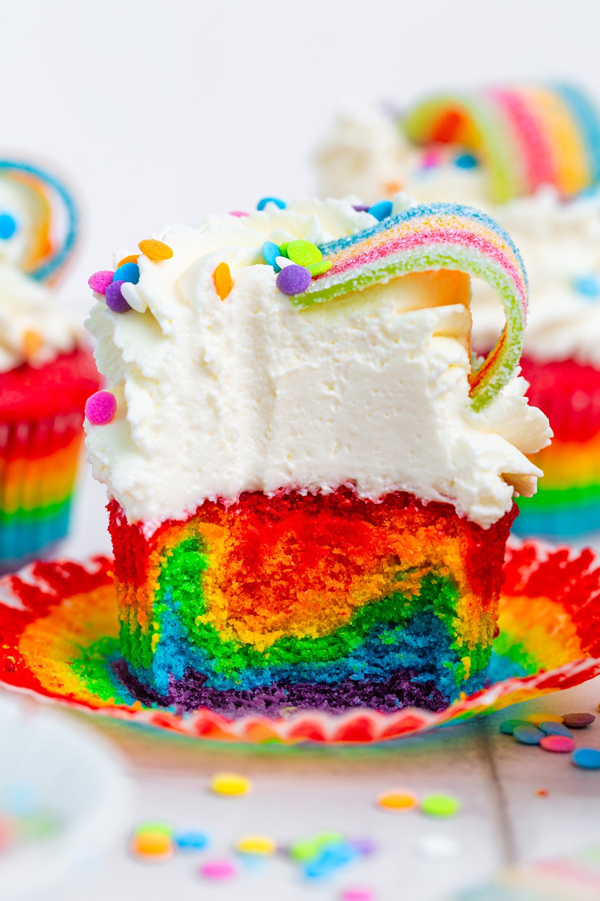 Rainbow cupcakes cut open on a table showing colorful layers