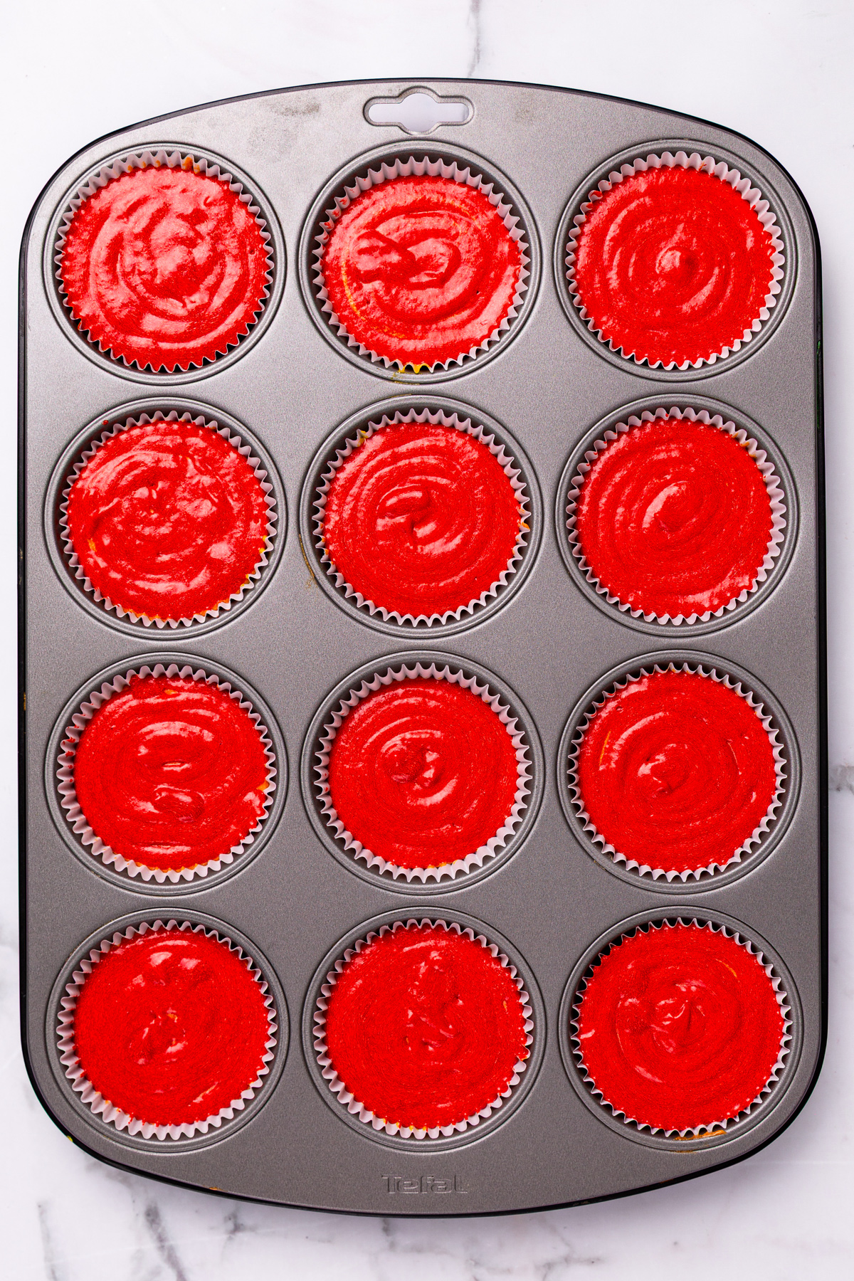 Muffin tin with rainbow cupcakes batter before baking