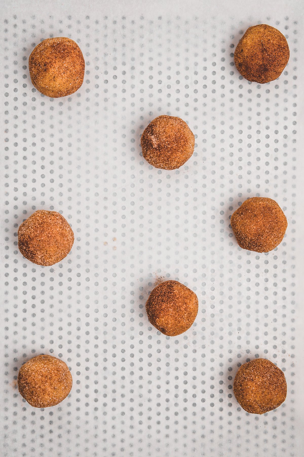 Unbaked snickerdoodle dough balls on a parchment lined baking sheet