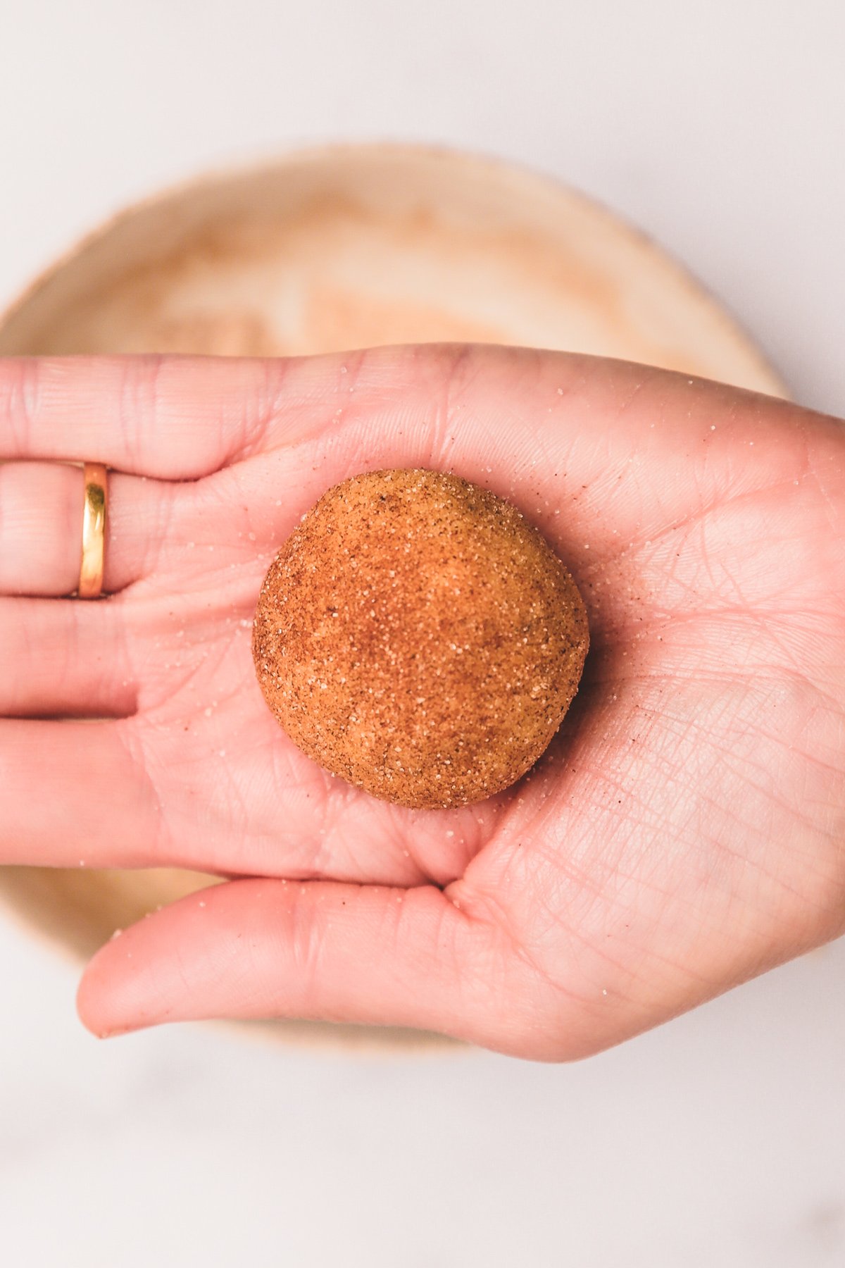 Hand rolling a snickerdoodle cookie dough ball in cinnamon sugar