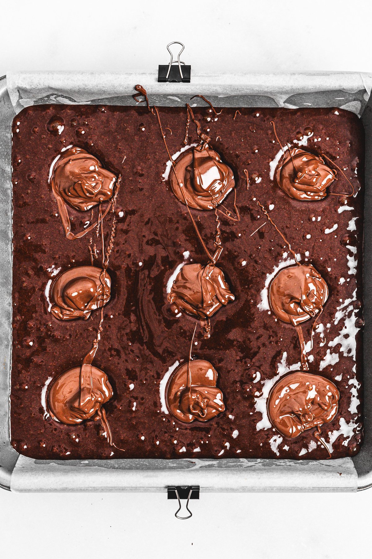 Nutella brownie batter in pan with spoonfuls of Nutella for swirl