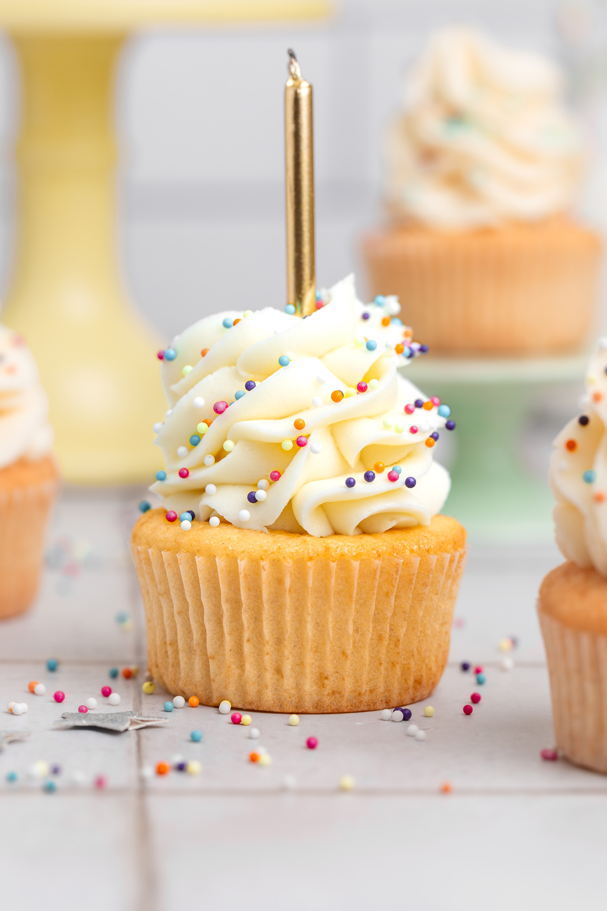 birthday cupcakes with vanilla buttercream frosting and colorful sprinkles on a table with a candle