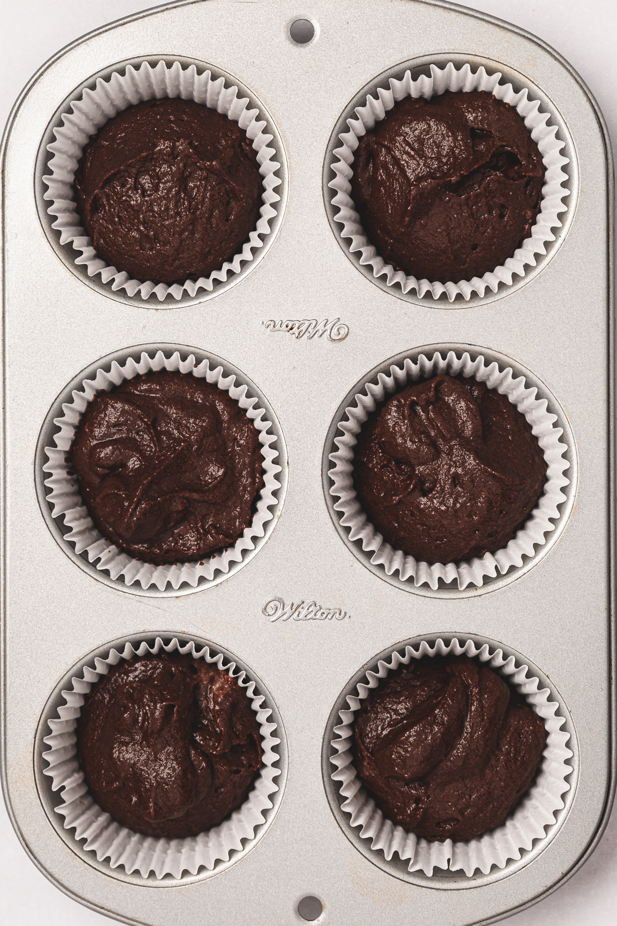 6 chocolate cupcakes before baking in a cupcake pan