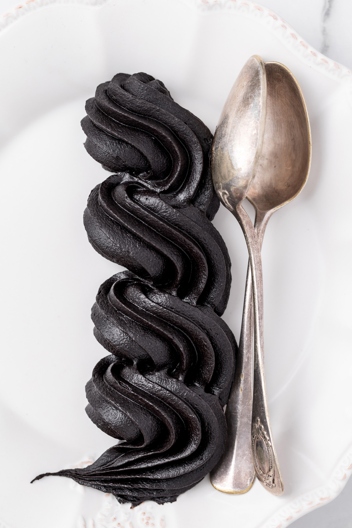 Black buttercream frosting piped beside vintage spoons